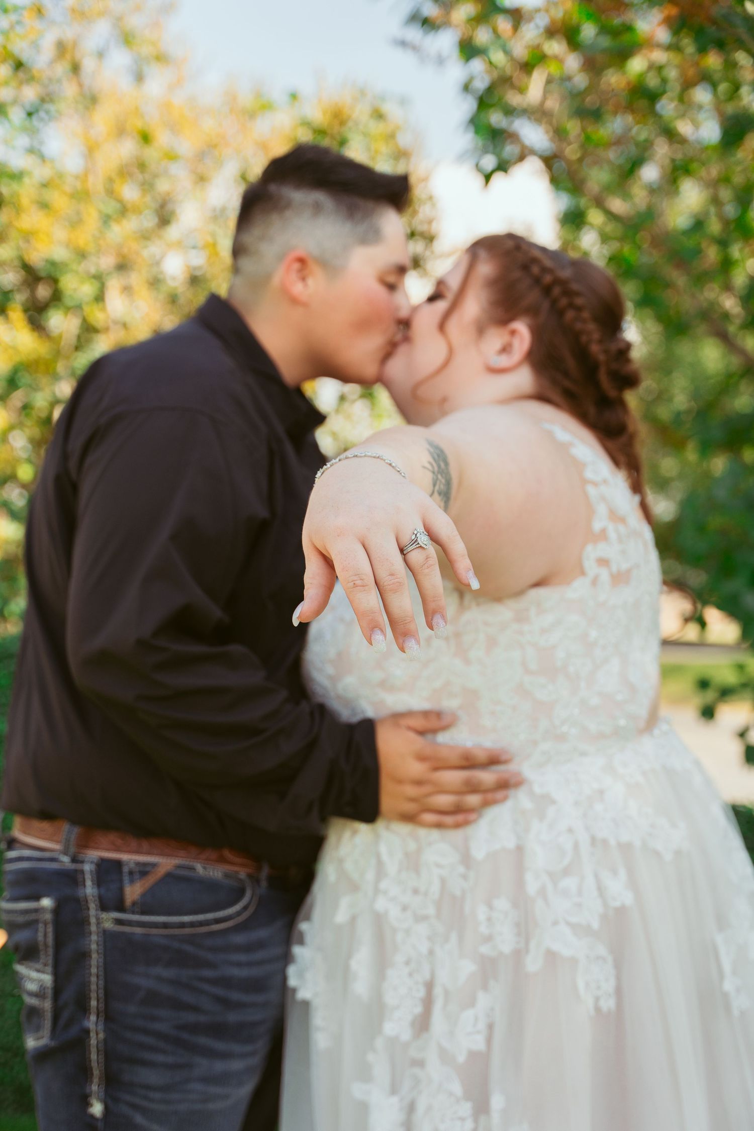 A tender wedding moment captured as a couple shares a kiss against a backdrop of fall trees.