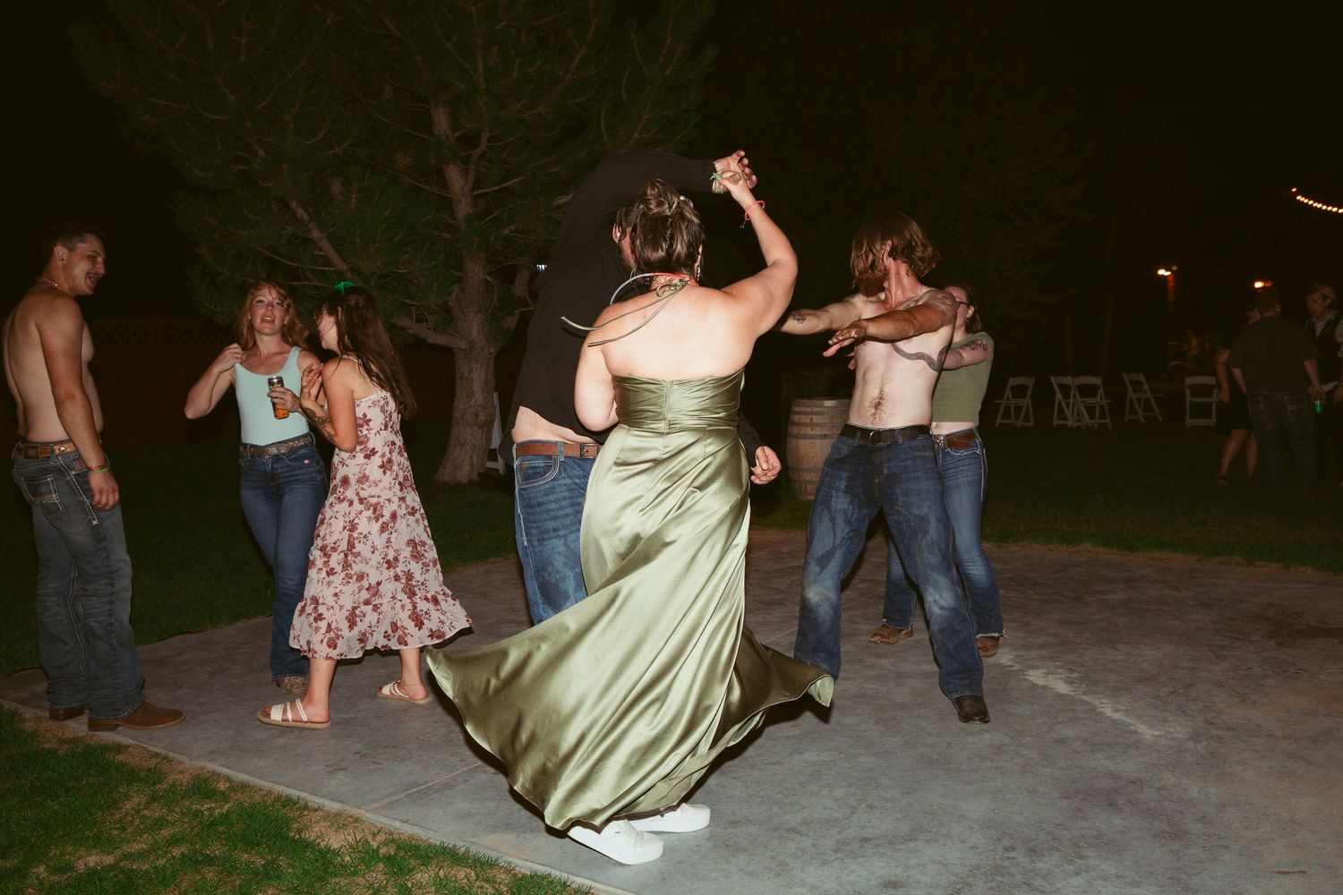 Wedding party members dance and celebrate on an outdoor patio during evening festivities.