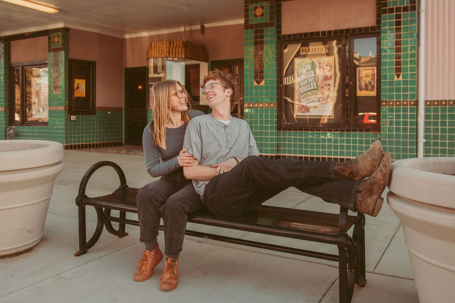 A couple sits together on a bench in a subway station with green tiled walls and white columns.