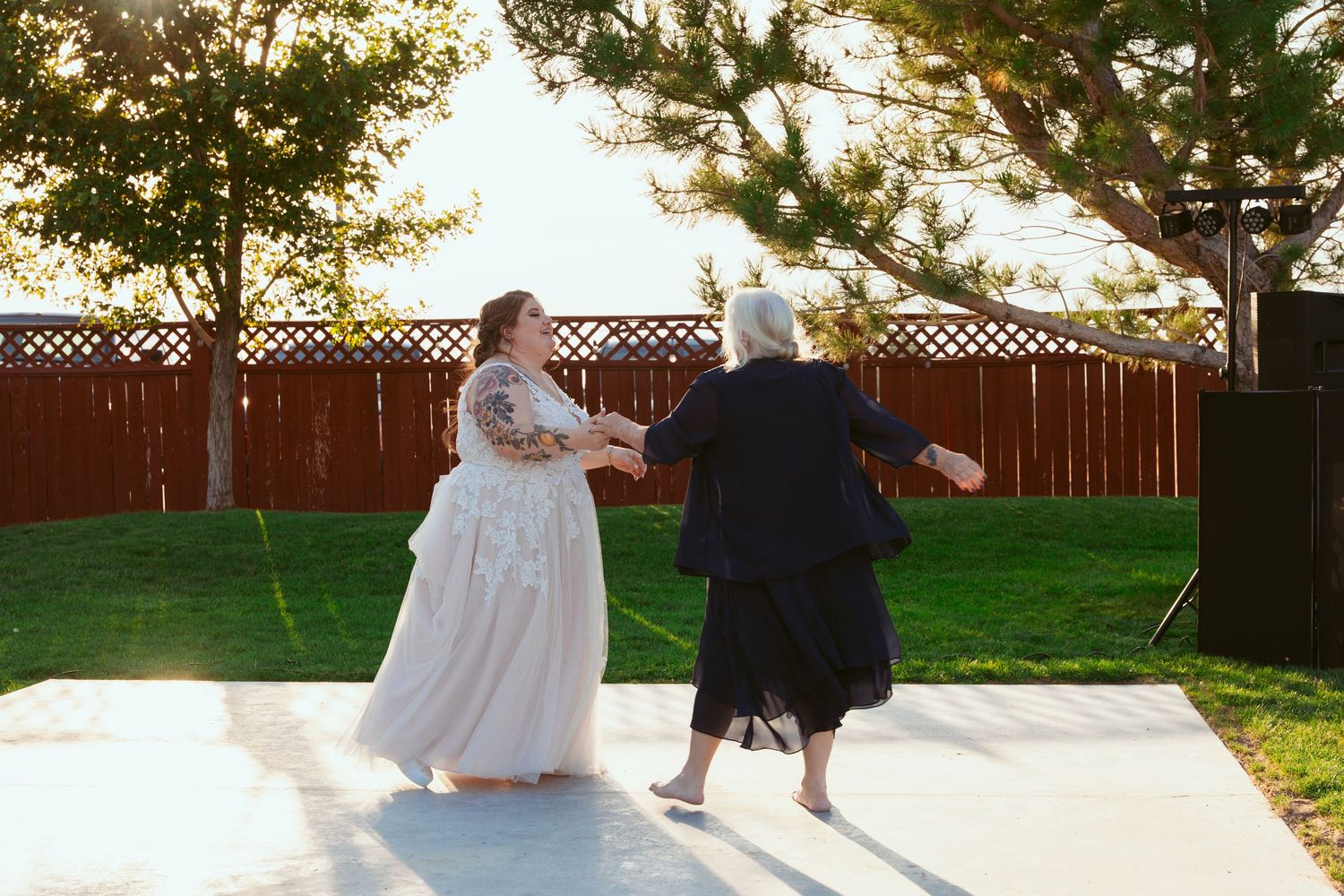 Two people dance together on an outdoor patio during a wedding reception at sunset.