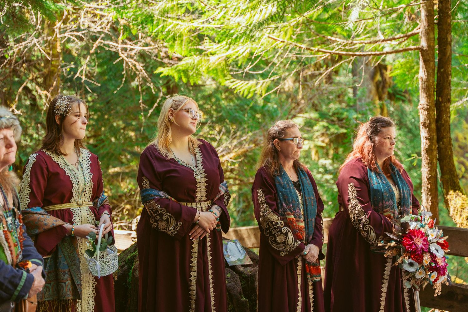 Wedding attendants in medieval-style attire stand in a forest setting.