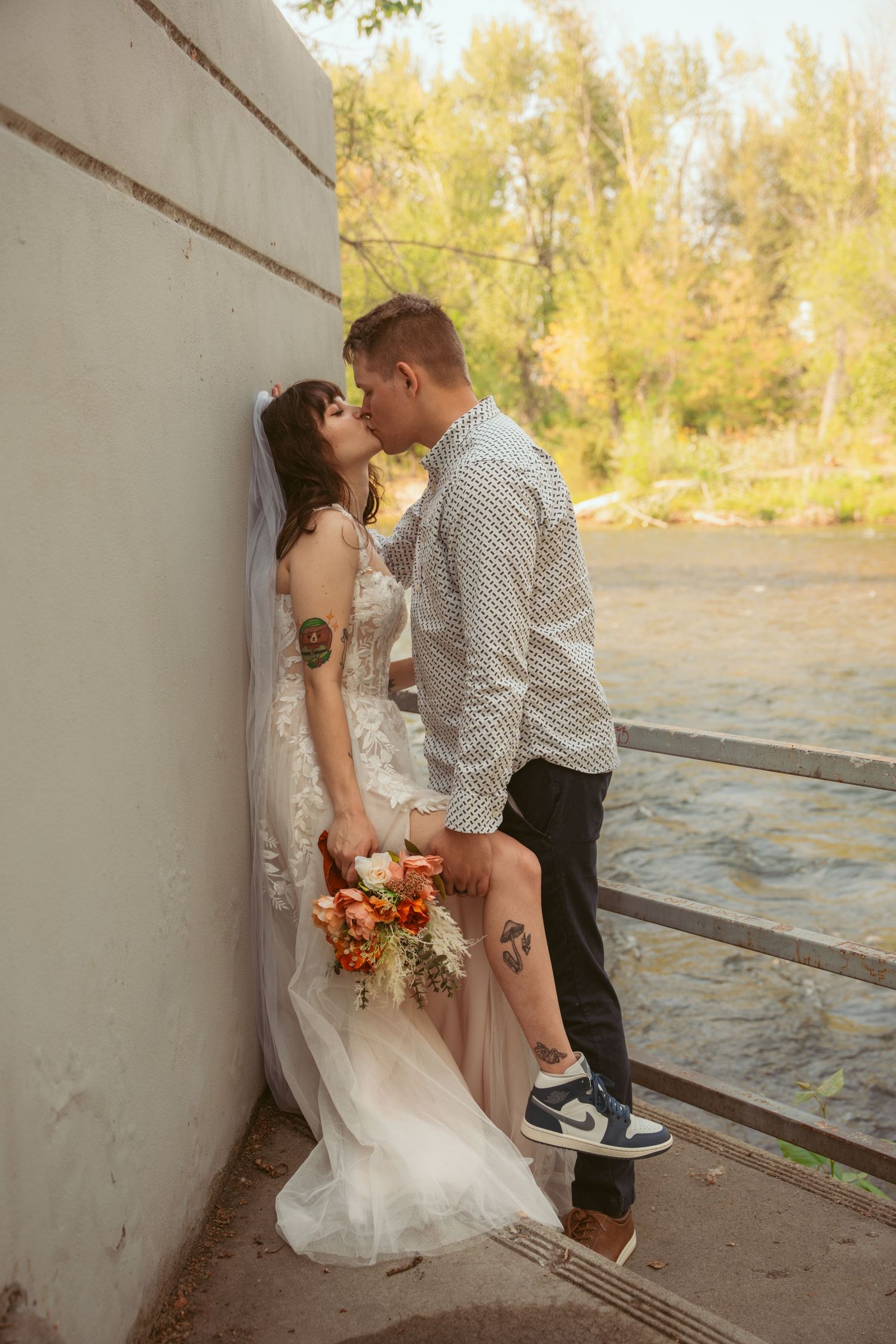 A romantic wedding photo against a wall with autumn trees in the background.
