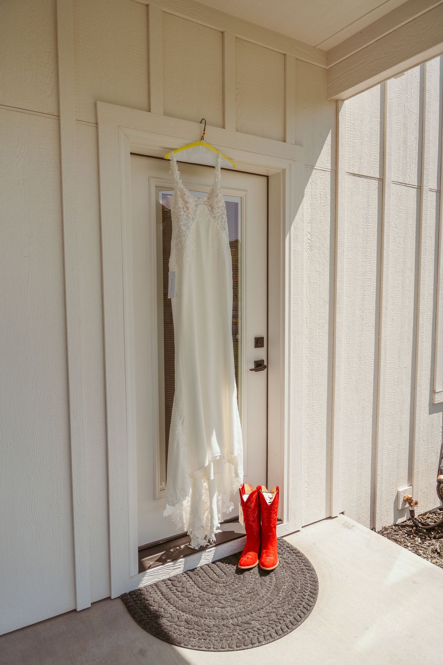 White wedding dress hanging in a bright room with red boots visible.
