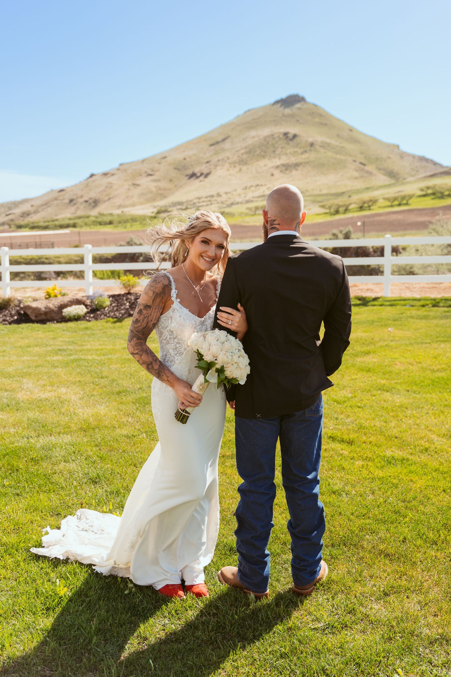 Wedding couple walking together on grassy hillside with mountain views.