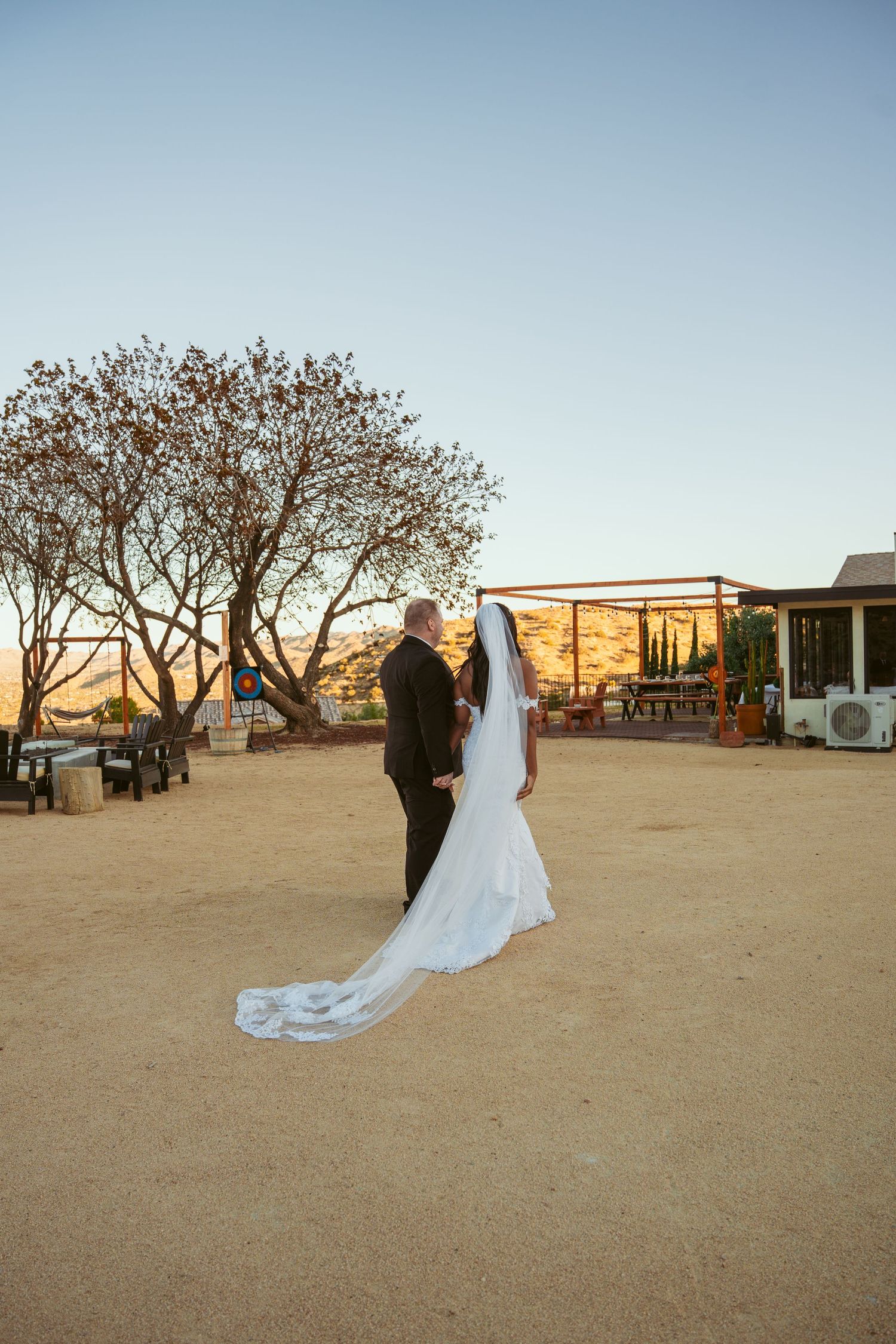 Wide view of a desert wedding venue with trees and mountains during golden hour.