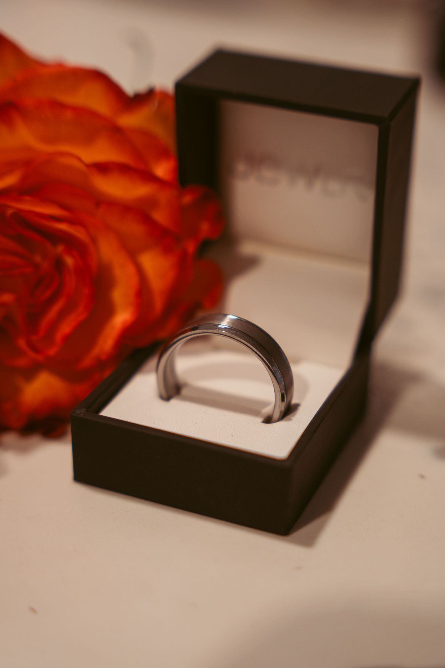 An elegant engagement ring displayed in a black jewelry box with an orange rose accent.