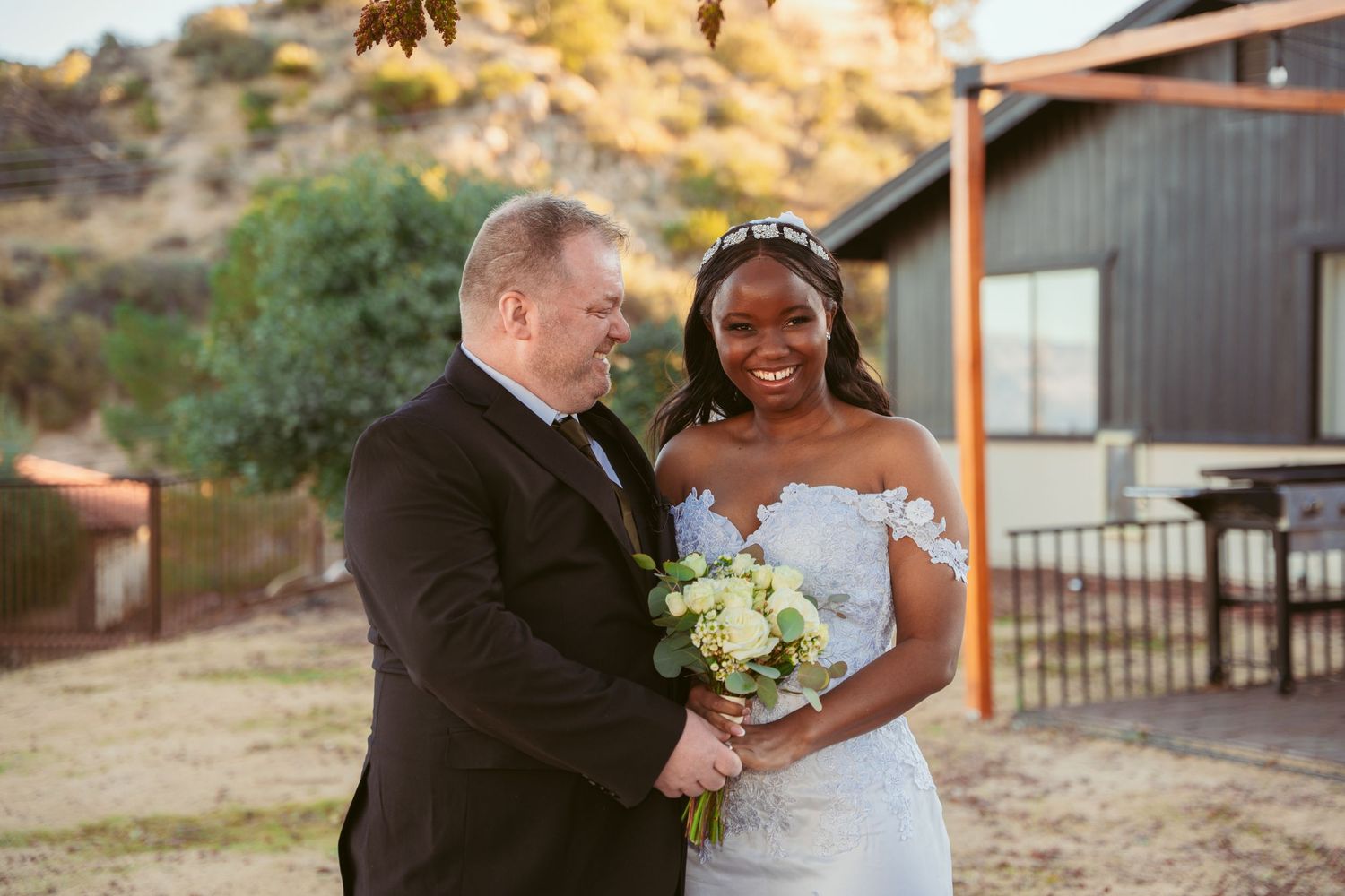 A wedding couple poses together in front of a desert landscape with mountains in the background.