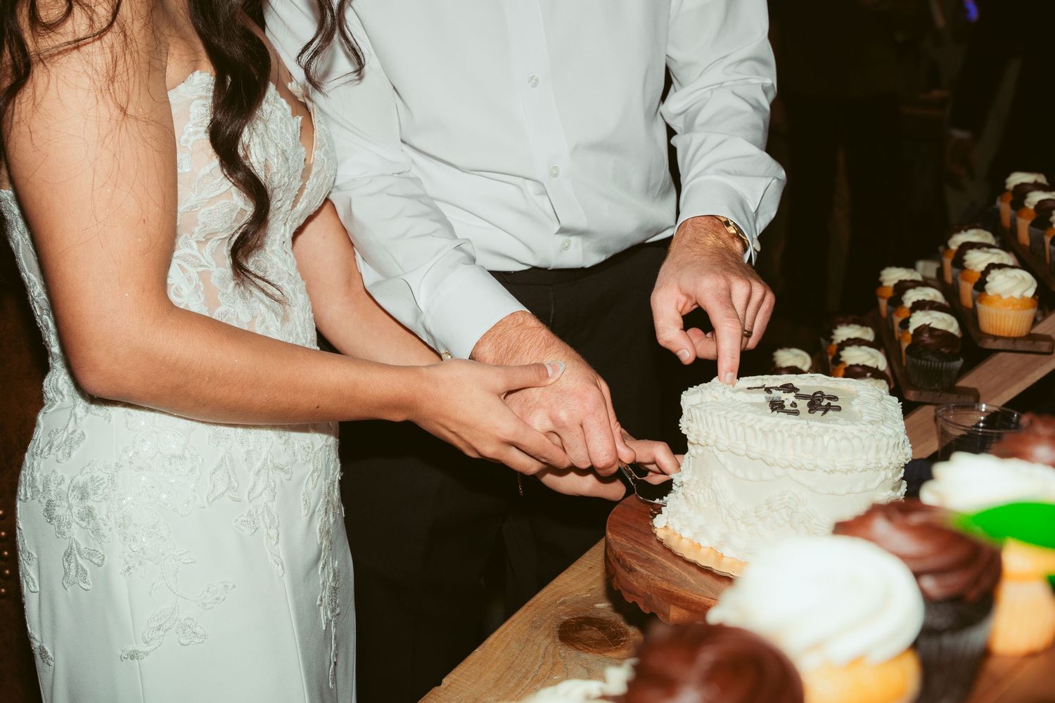Couple cutting their white wedding cake during reception celebration.