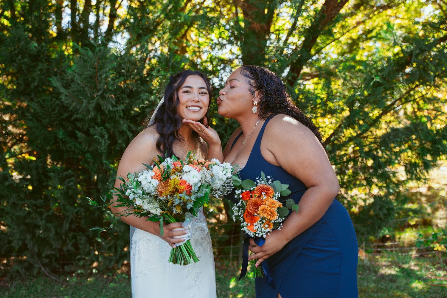Wedding group poses with orange bouquets against golden sunlit foliage in outdoor setting.