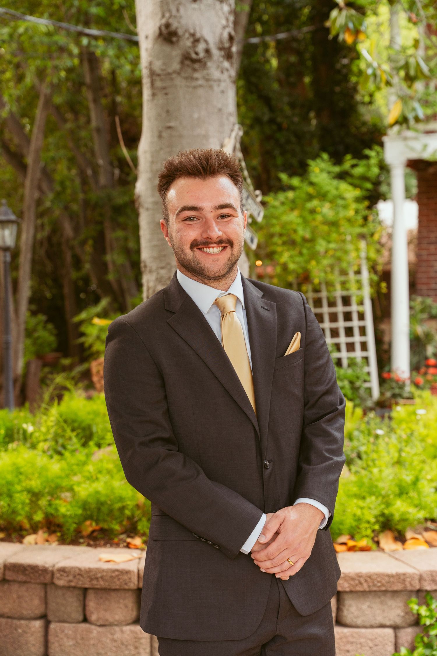 Wedding portraits of a groom in a black suit with yellow tie posing in a garden setting.