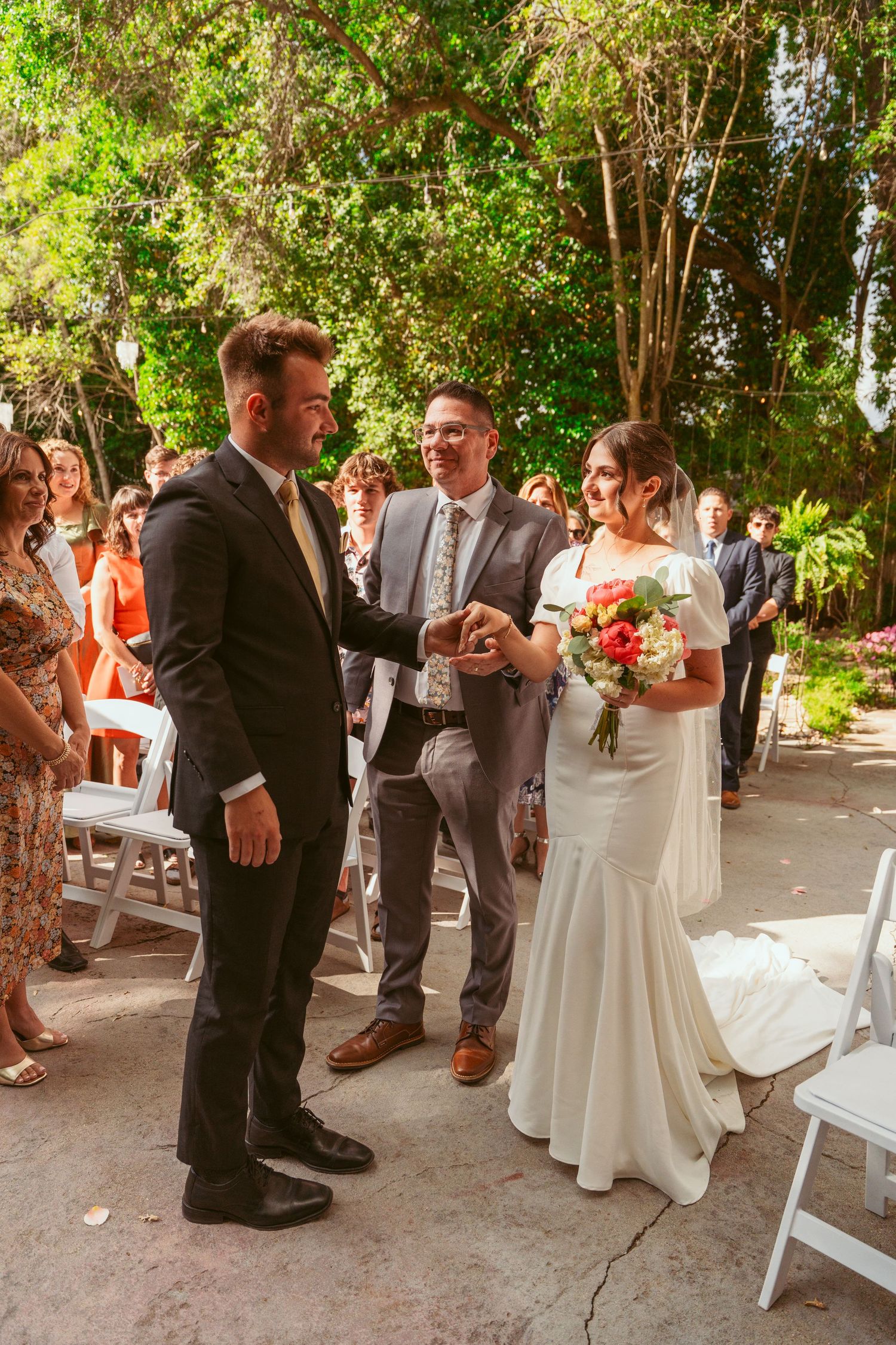 Wedding guests gather around the couple during an outdoor garden celebration.