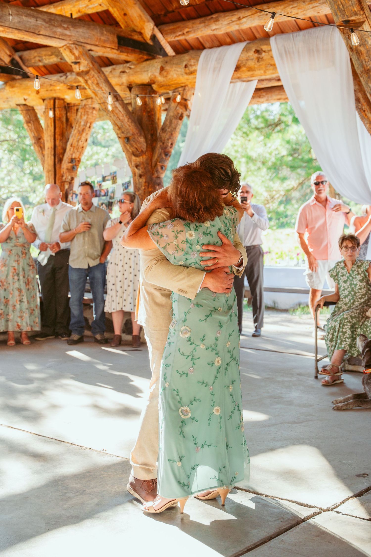 Couples dance together under a timber-framed pavilion with white draping and natural lighting.