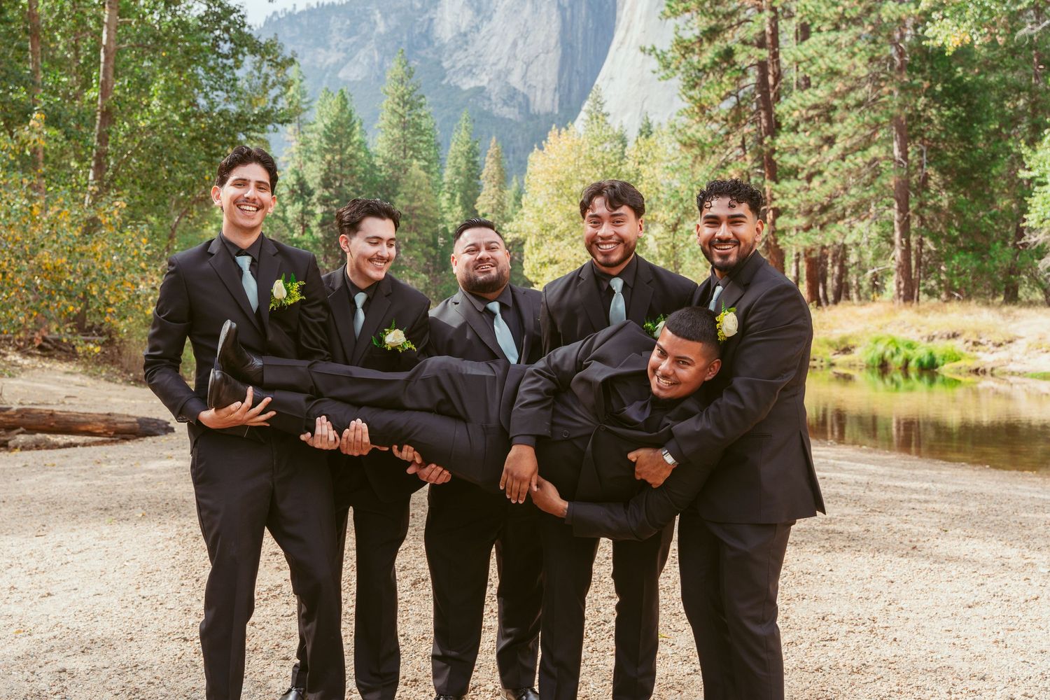 Groomsmen in black suits posing together outdoors with mountain scenery.