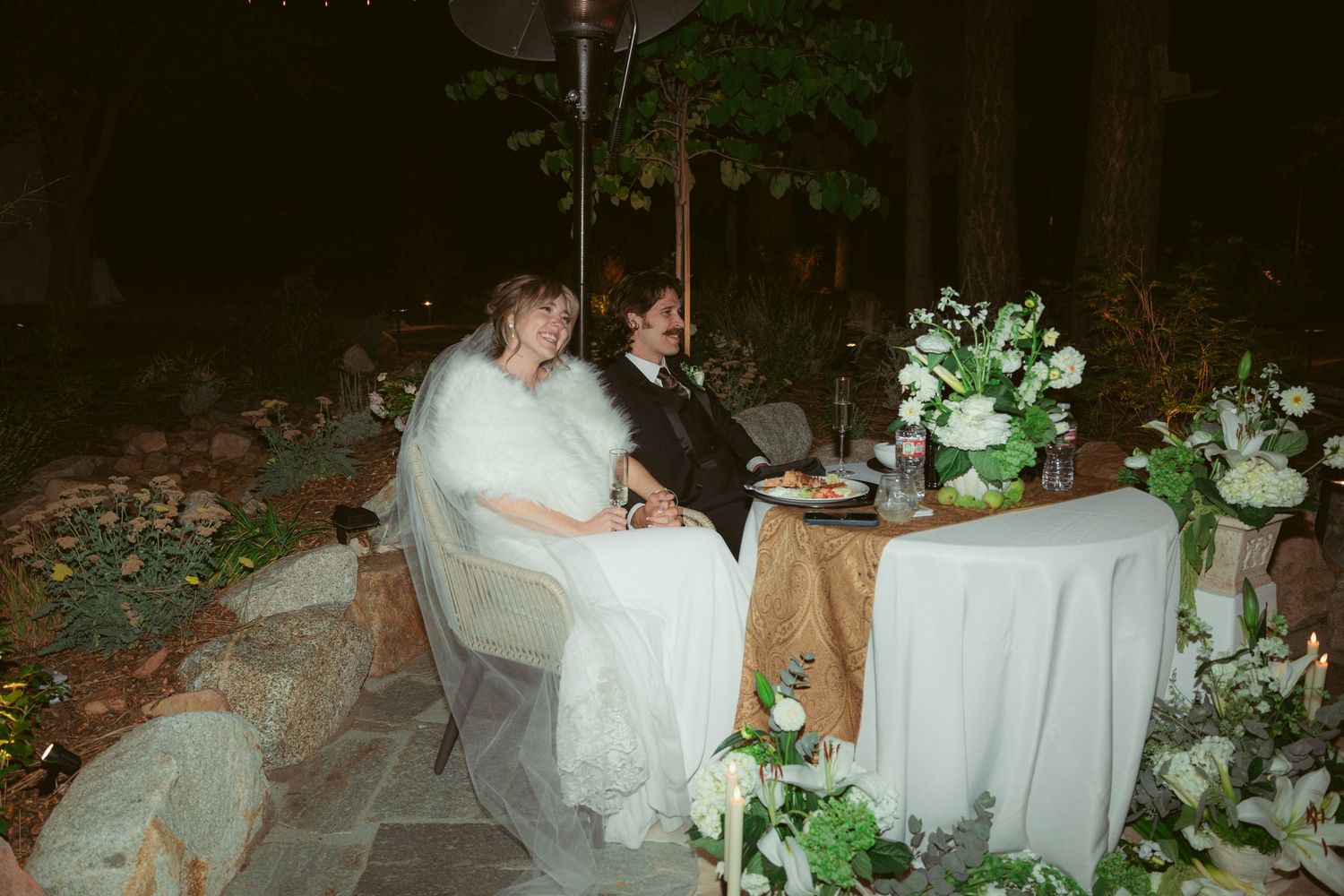 Bride in a flowing white gown seated at an elegantly decorated outdoor reception table.