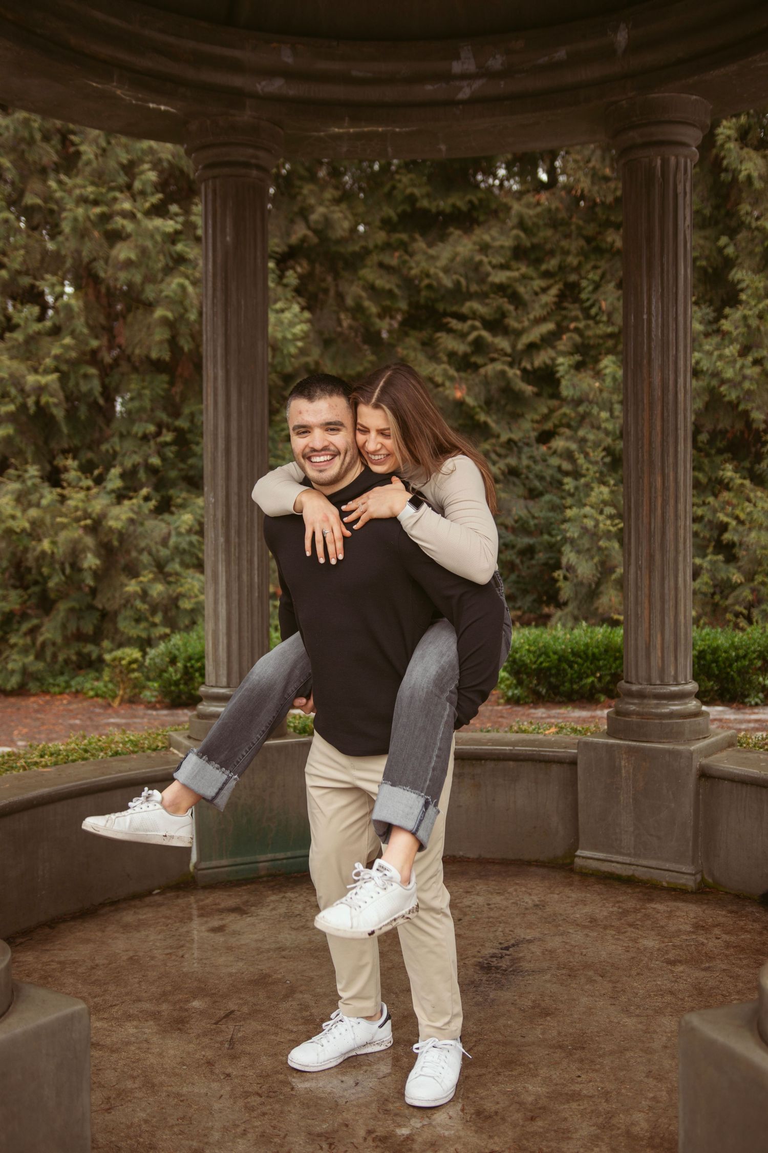 A couple sharing a playful piggyback moment in a garden gazebo.