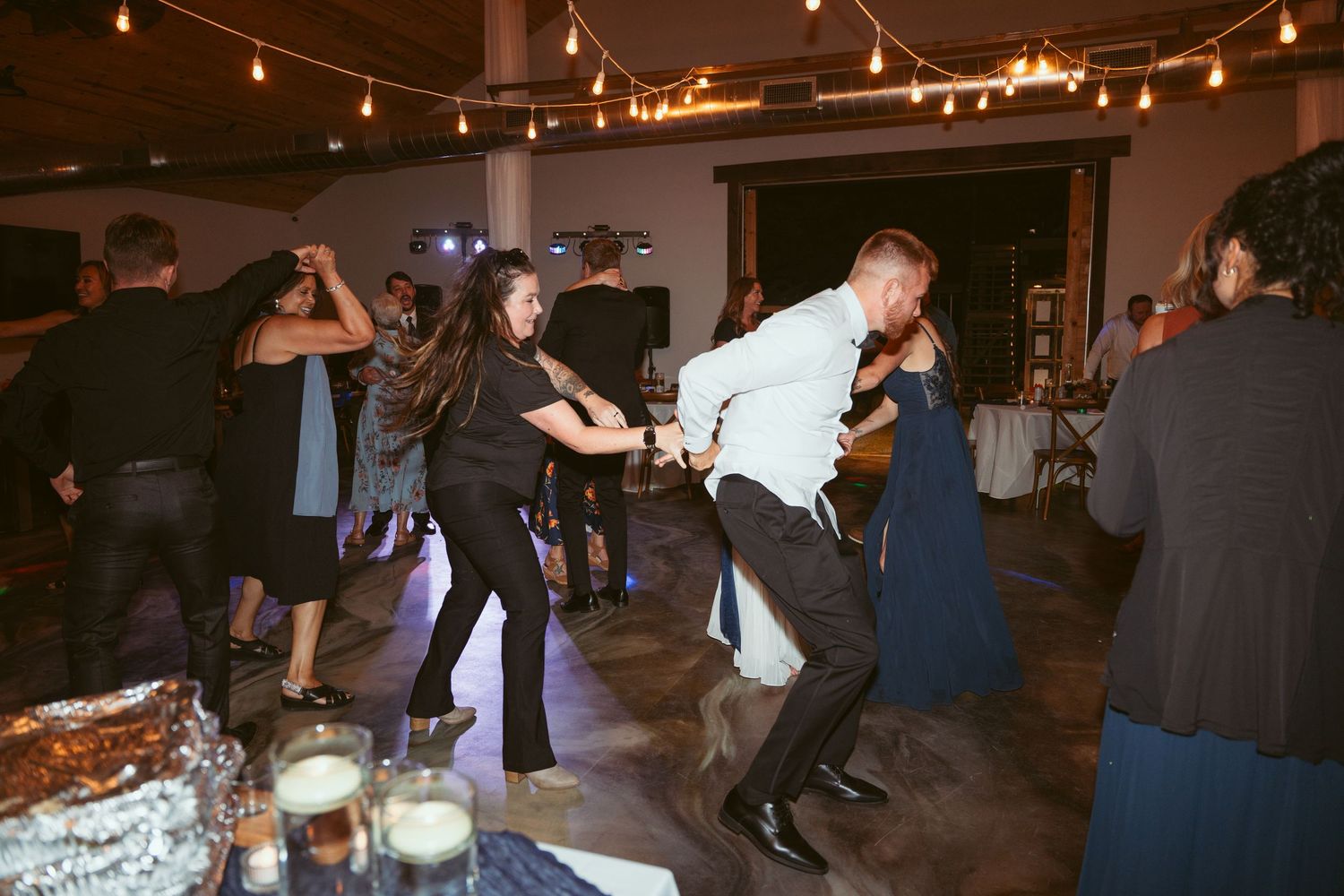 Dancers moving across the floor at a dimly lit indoor social gathering.