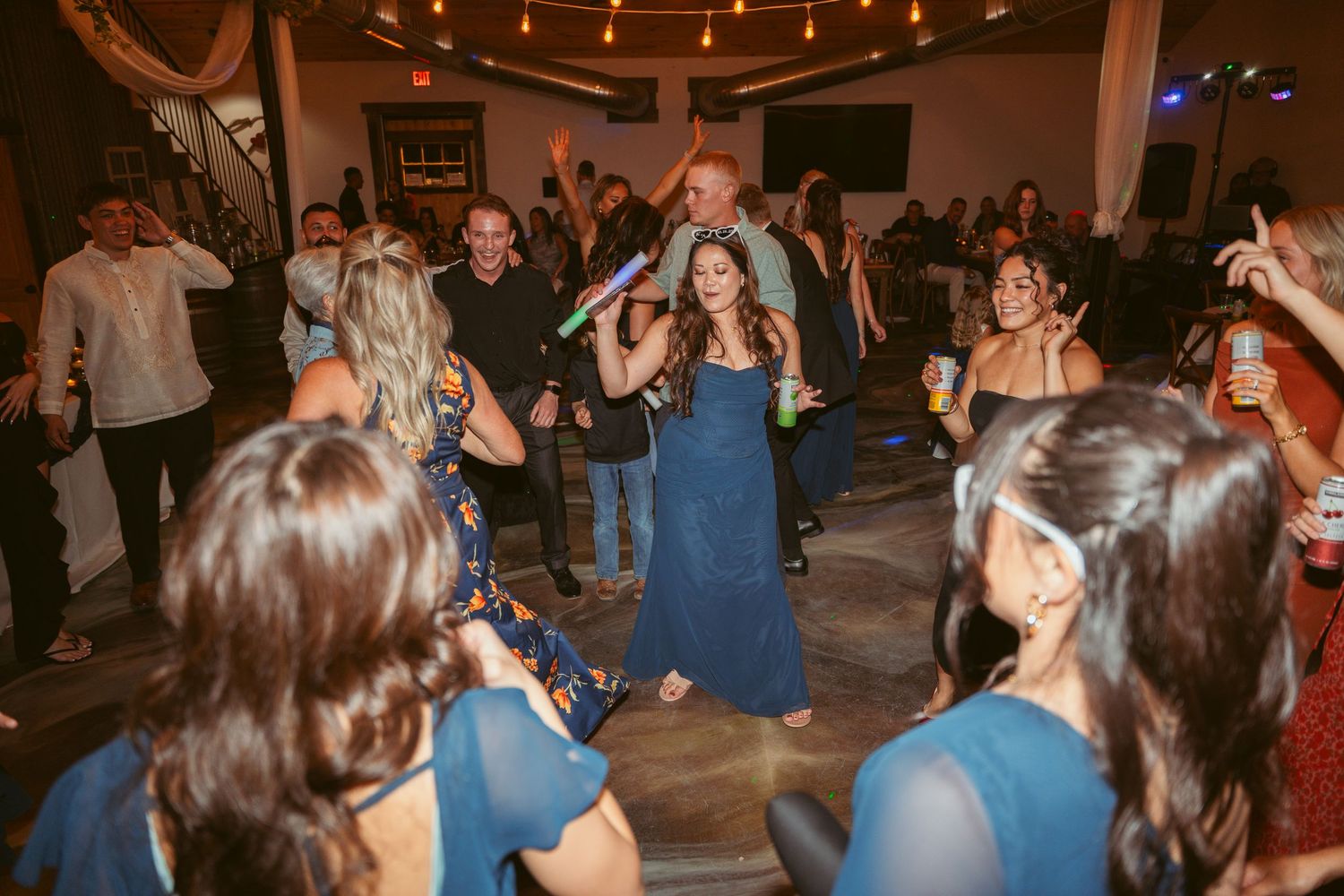 Guests in formal attire dancing together at an evening celebration with overhead string lighting.