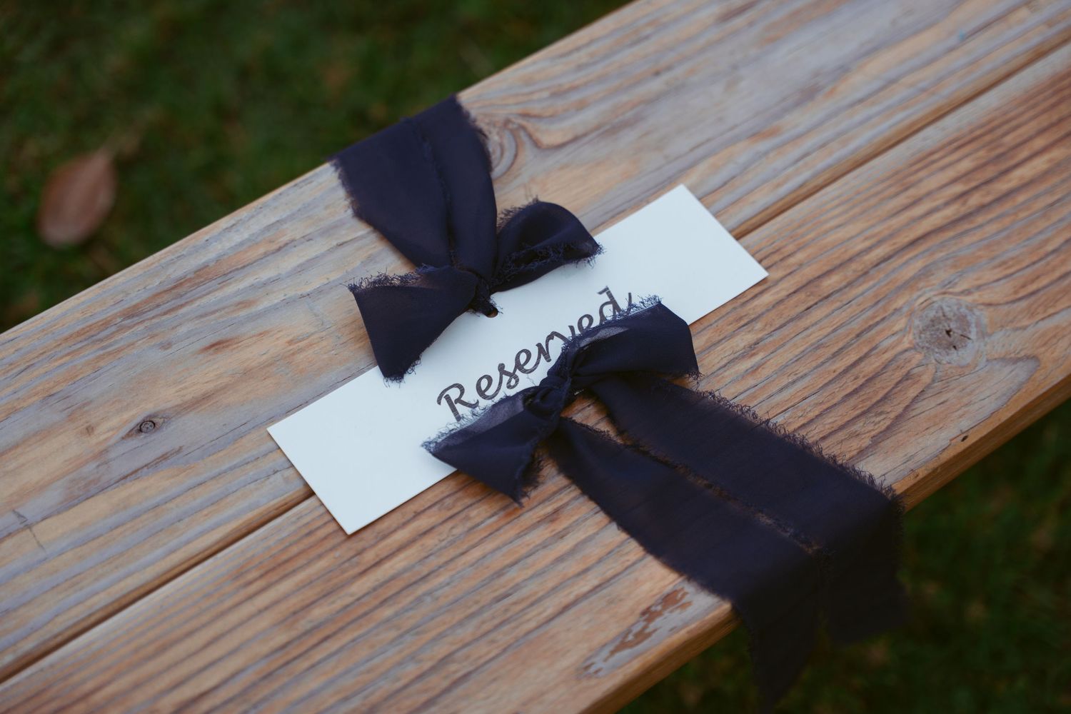 Reserved seating sign with black ribbon tied to wooden bench at outdoor venue.