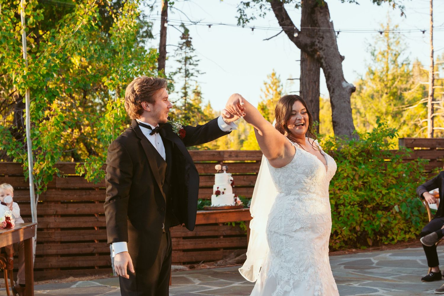 Couple performs choreographed dance moves on stone patio during outdoor wedding reception.