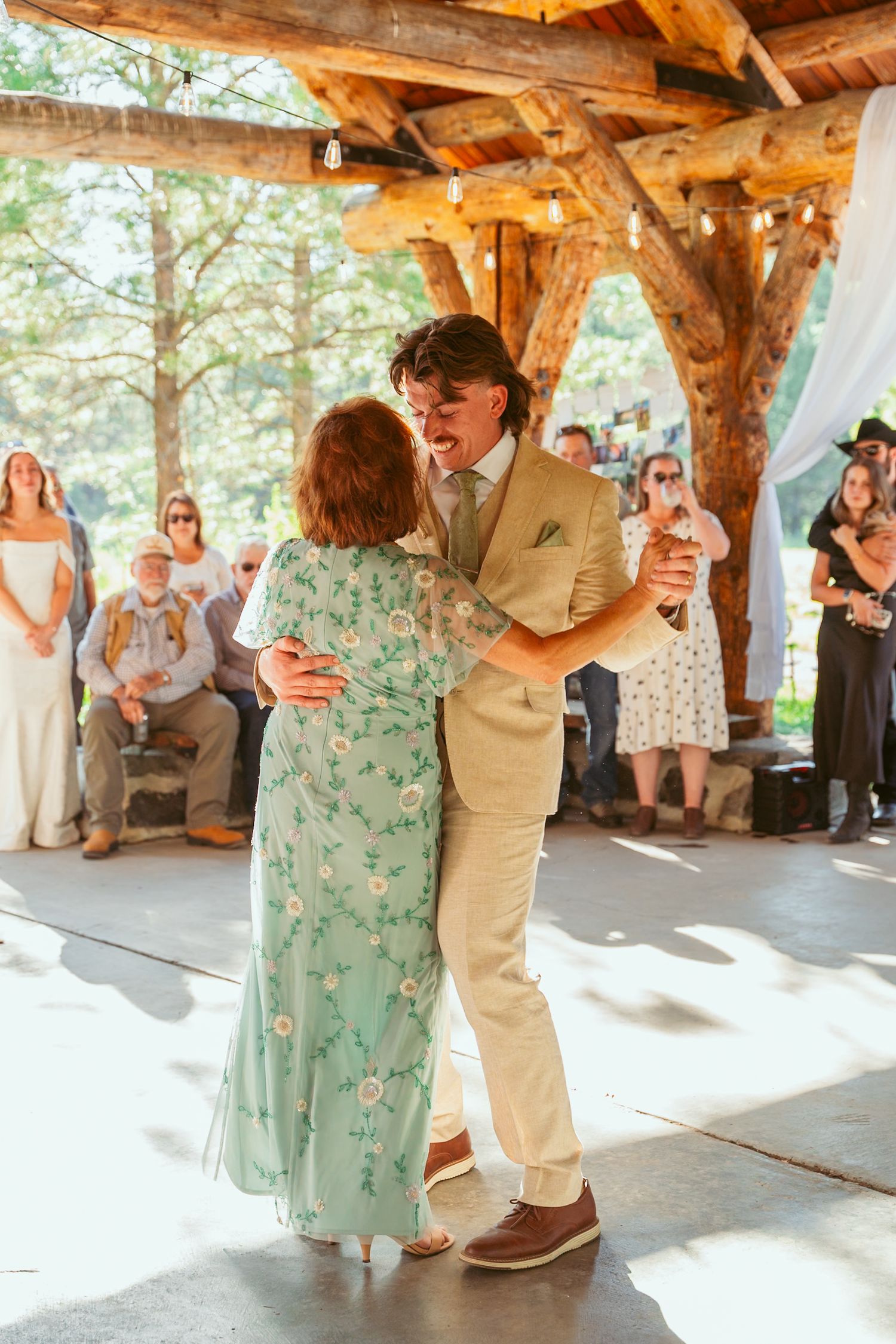 Wedding celebration with dancers performing under rustic wooden pavilion surrounded by guests.