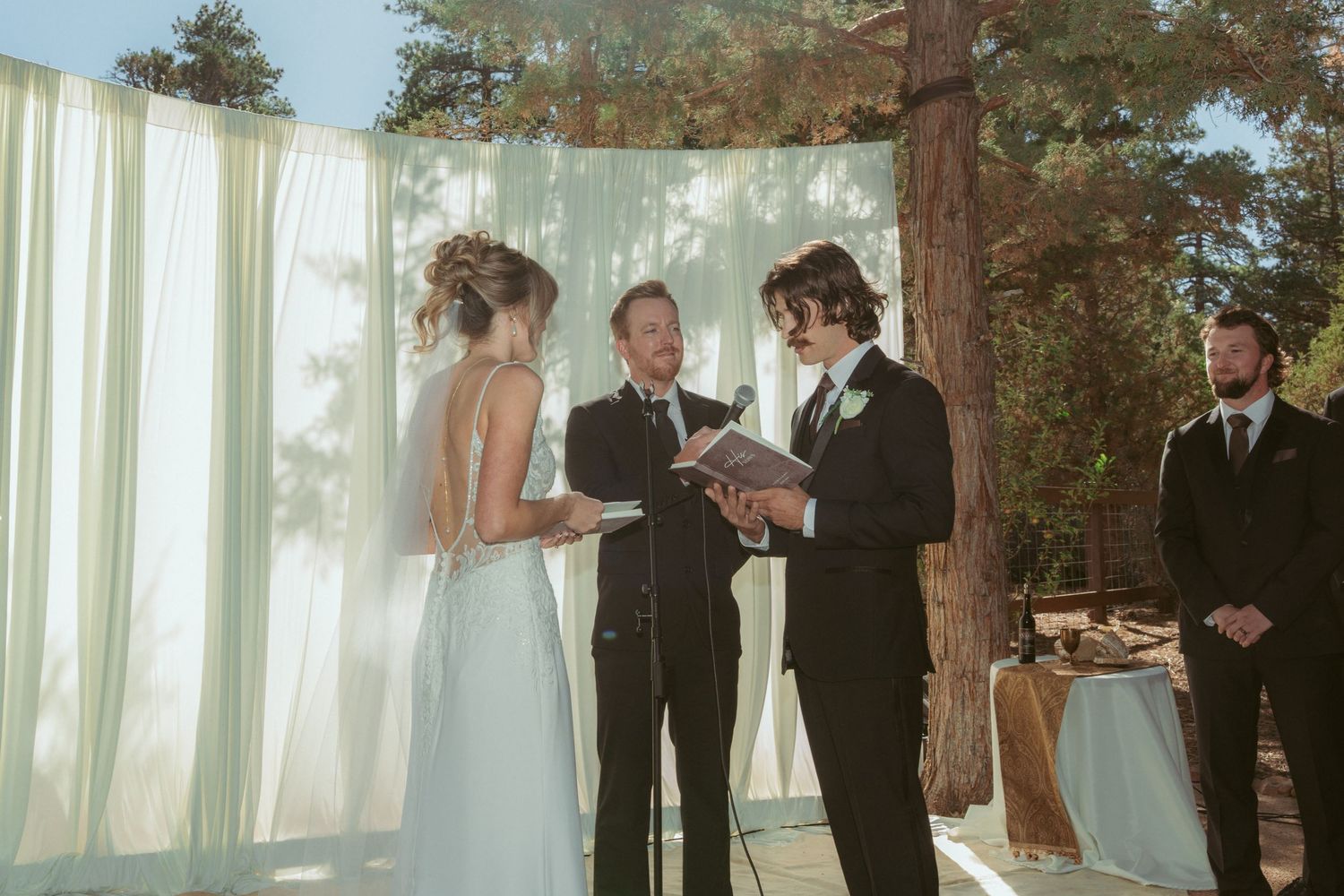 Outdoor forest wedding ceremony with white curtain backdrop and natural lighting.