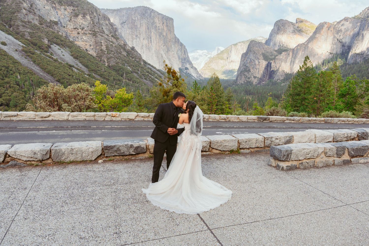 Wide panoramic view of a couple taking wedding photos with Yosemite's majestic valley walls.