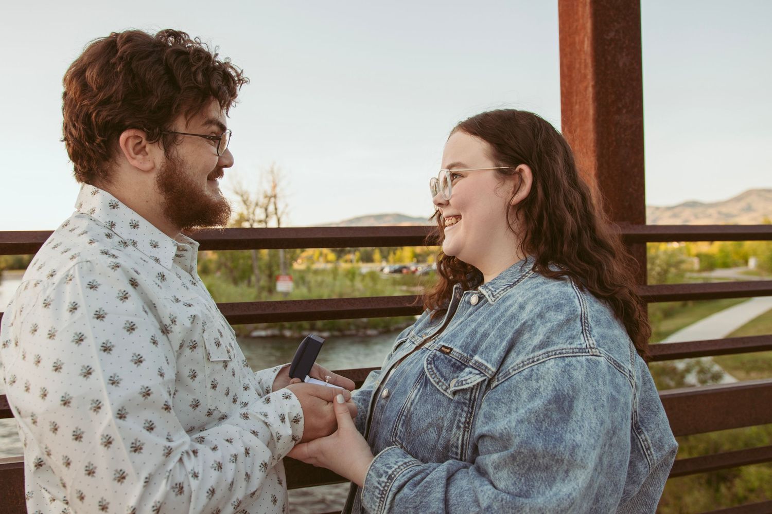 A couple laughs together during an outdoor proposal moment.