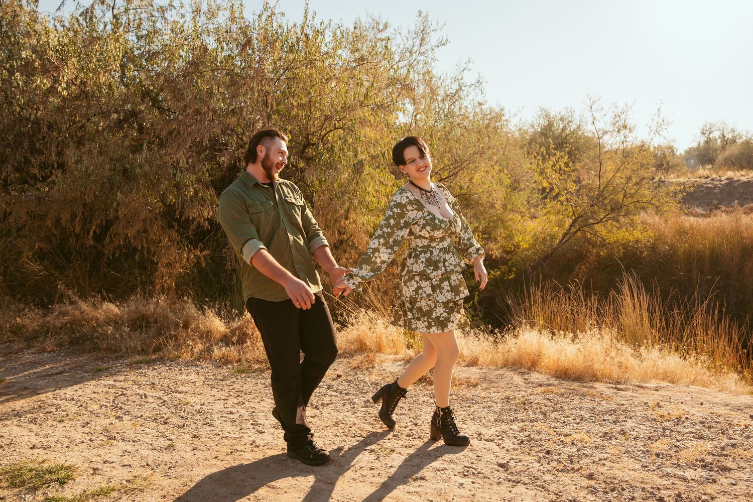 A playful couple dances together on a dirt path surrounded by autumn foliage.