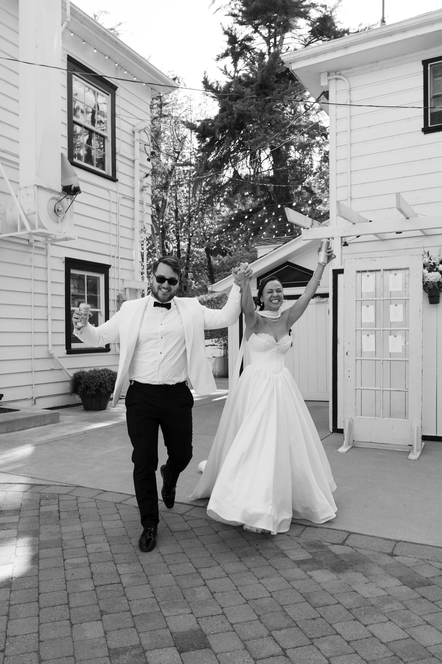 Wedding couple dances and spins joyfully outside a white building.