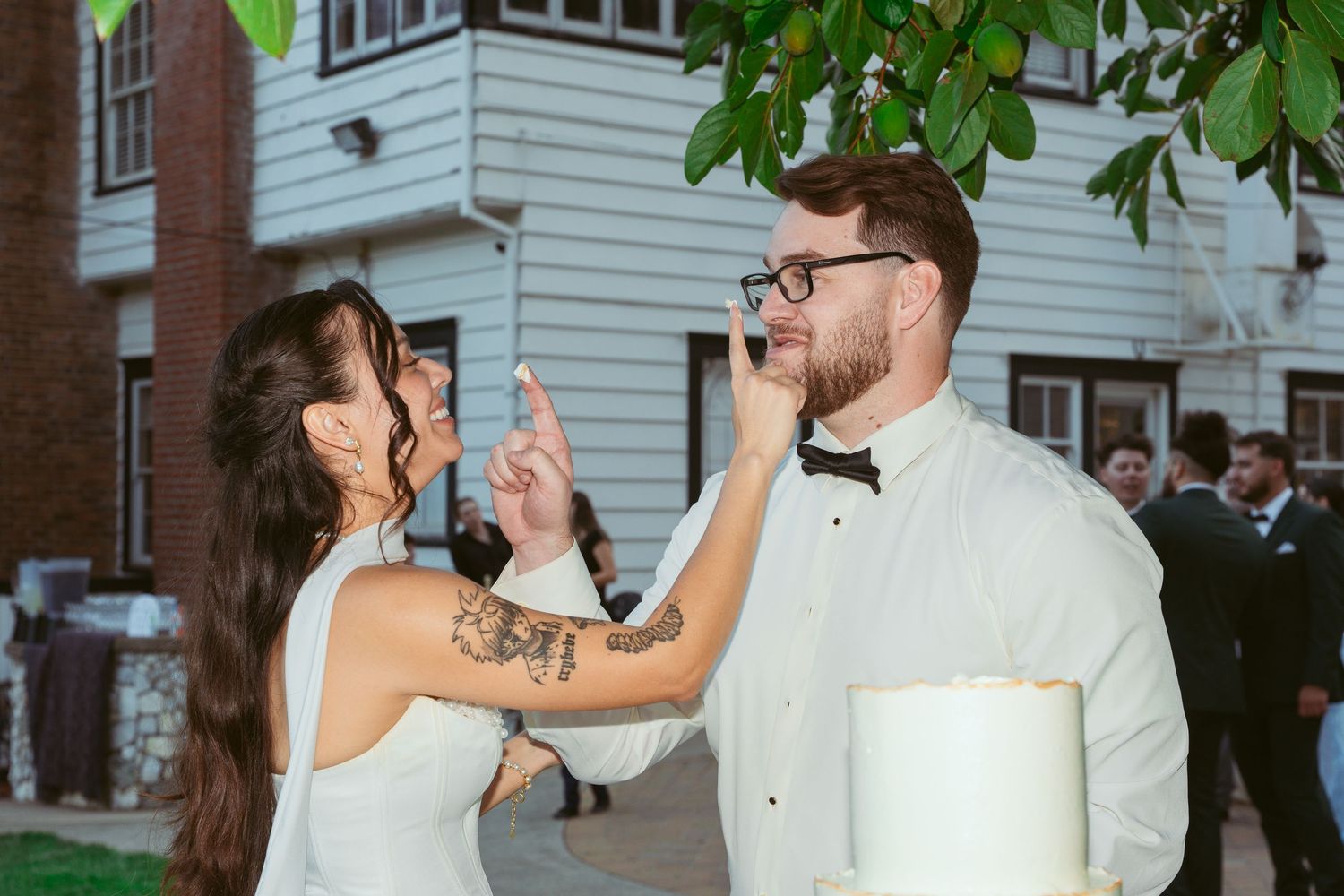 A couple shares a playful moment while cutting their wedding cake at an outdoor reception.