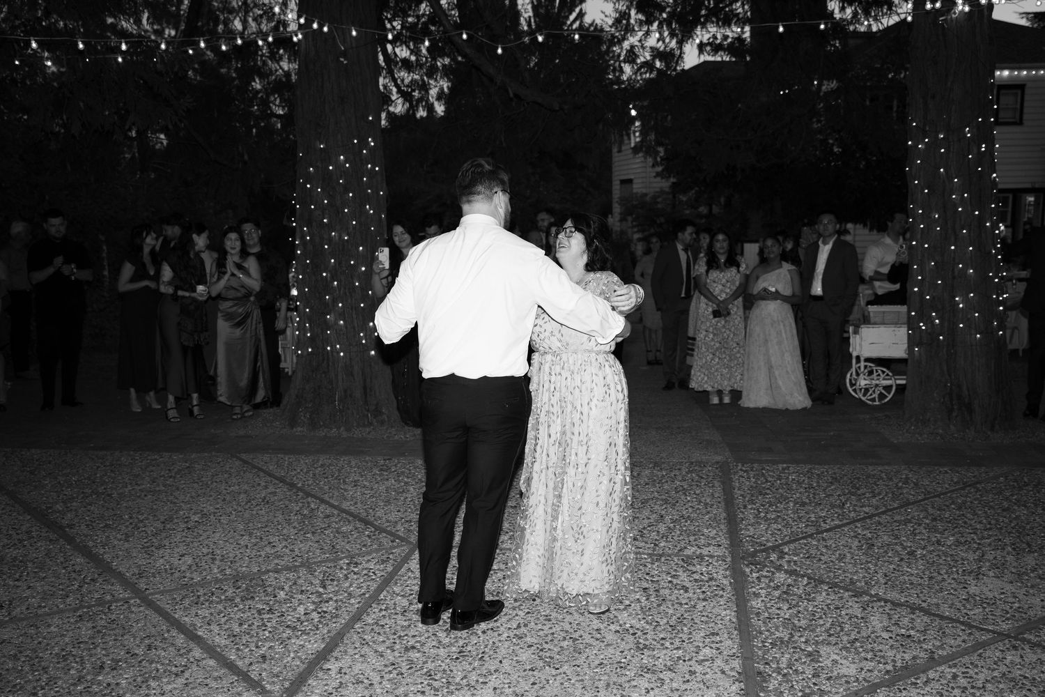People dancing at a wedding reception under twinkling lights at night.