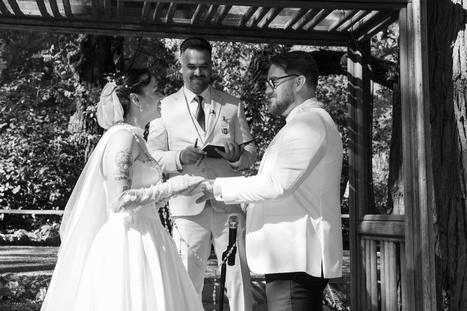 Black and white photo of wedding ceremony moments captured under a rustic wooden structure.