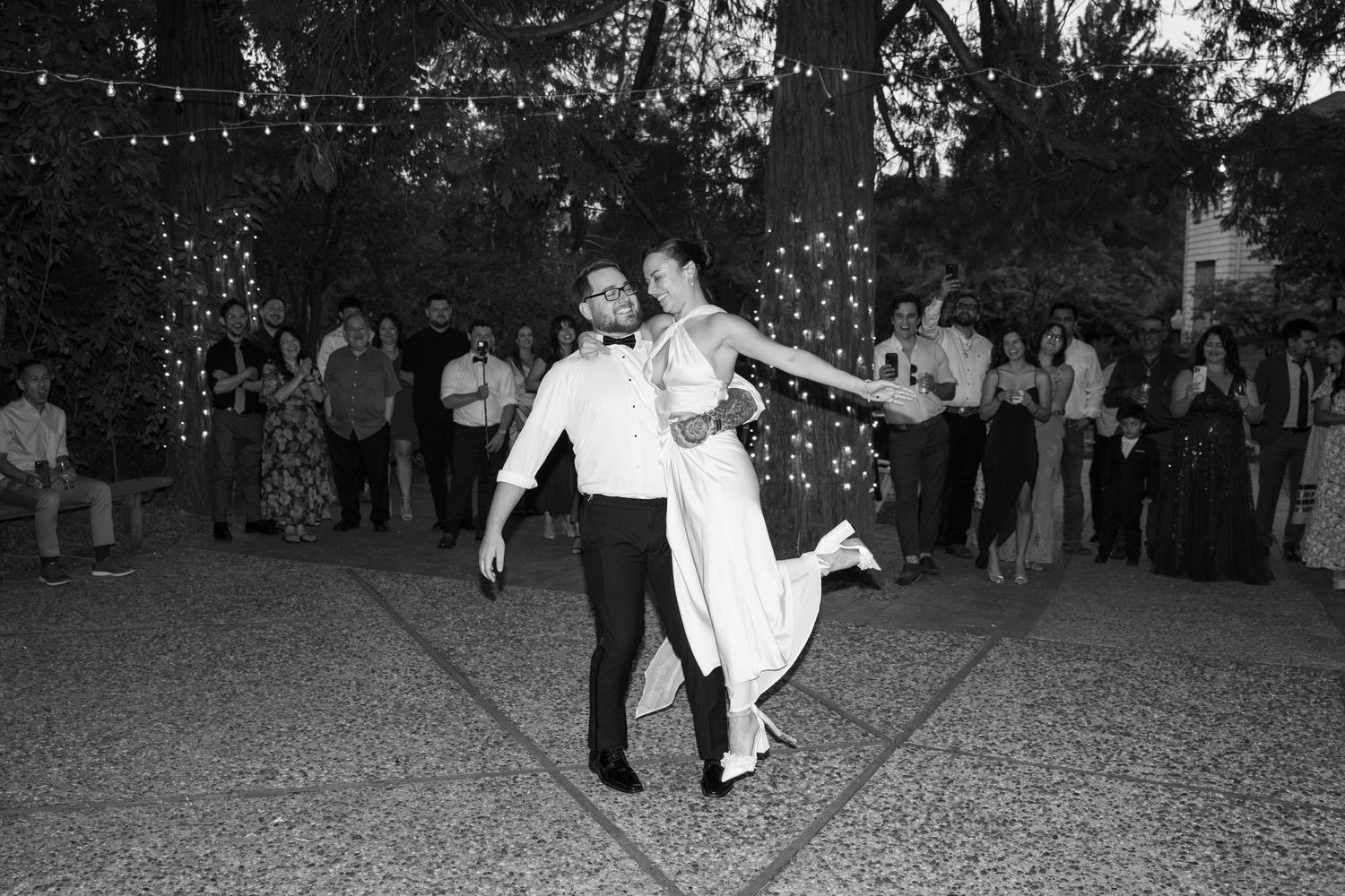 Wedding guests dance energetically on a dark dance floor during an evening reception celebration.