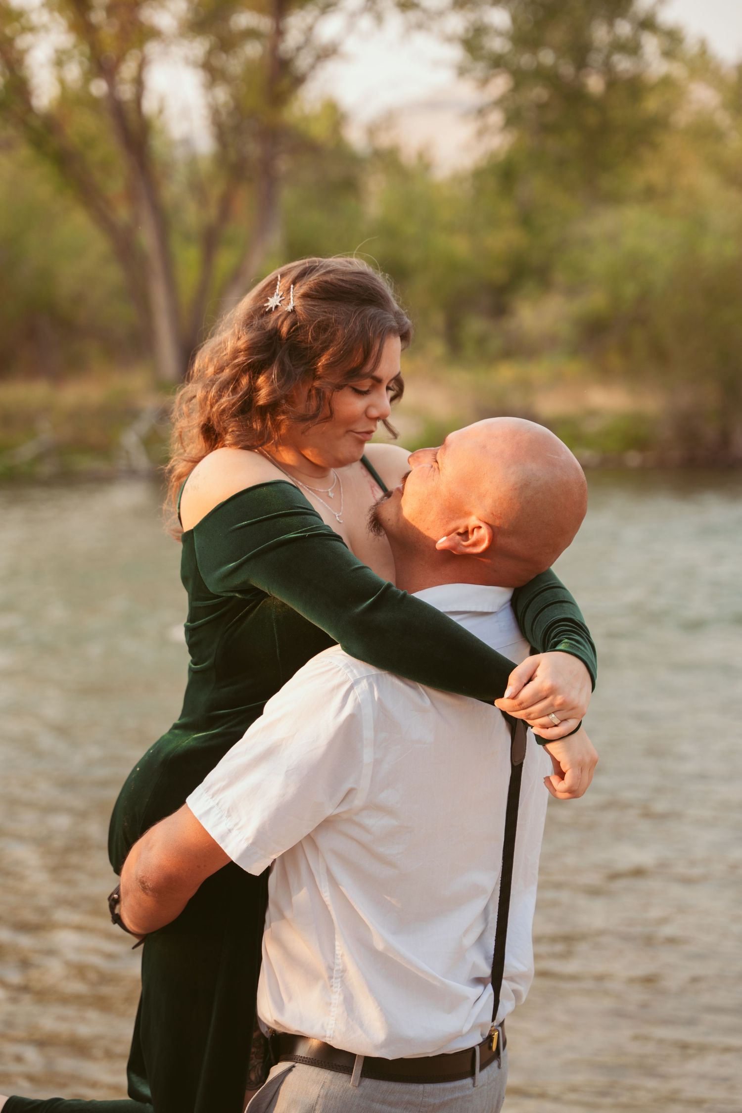 A couple embraces tenderly by a lake during golden hour.