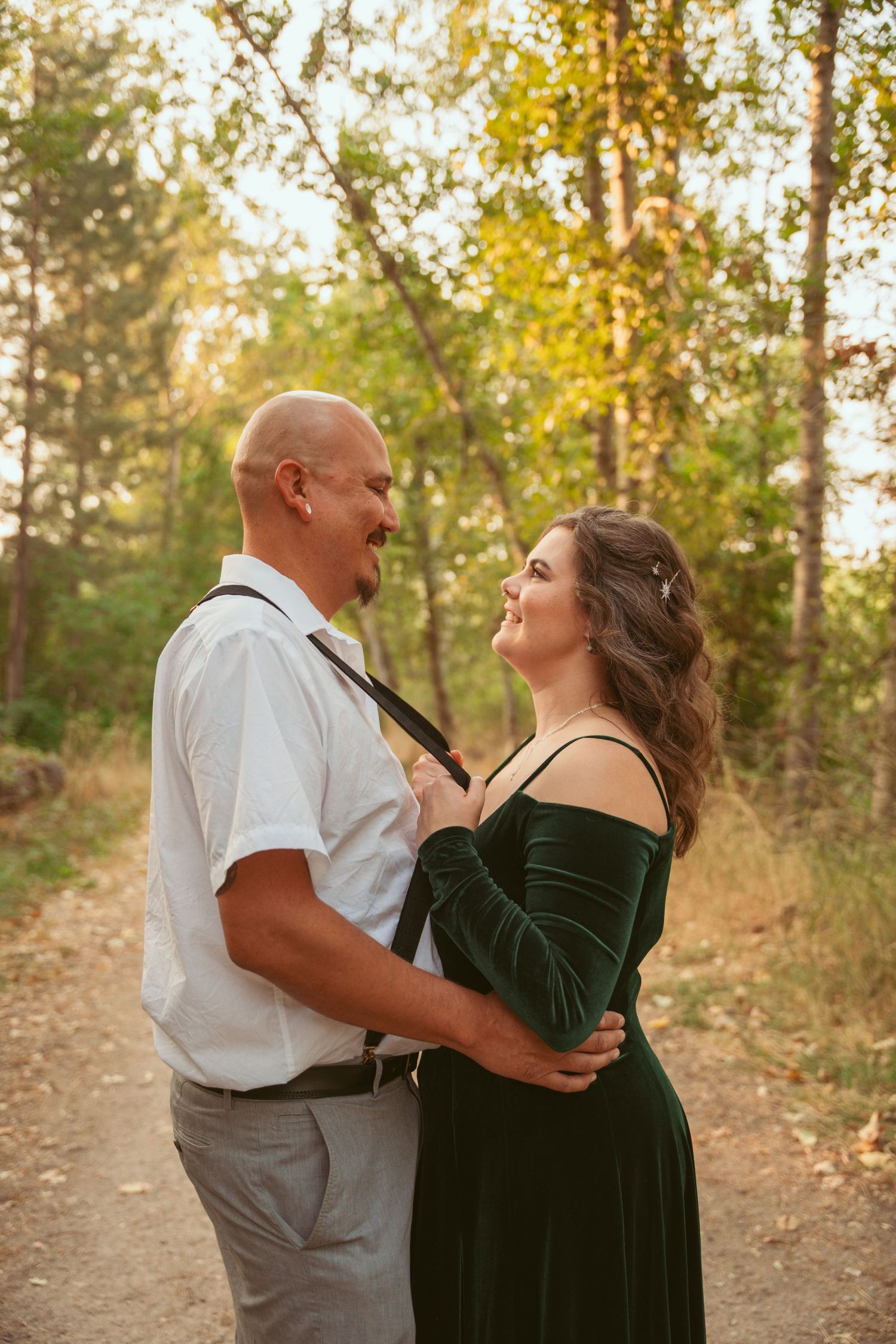Couple in formal attire dancing together on a wooded path at sunset.