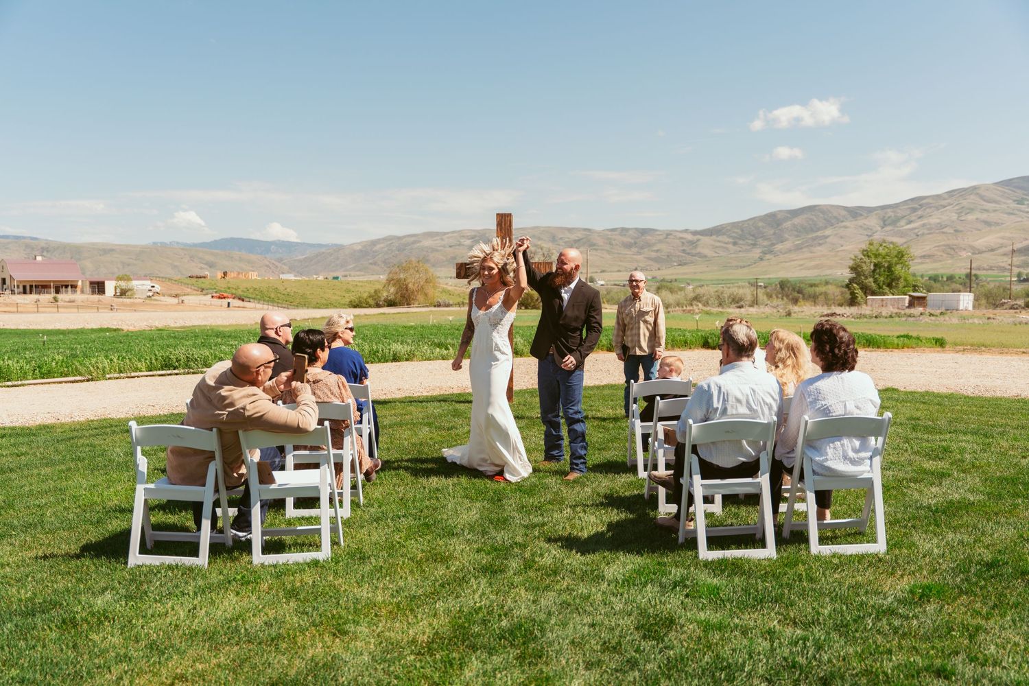 Wedding guests seated in white chairs watch the ceremony on a sunny day with mountains in view.