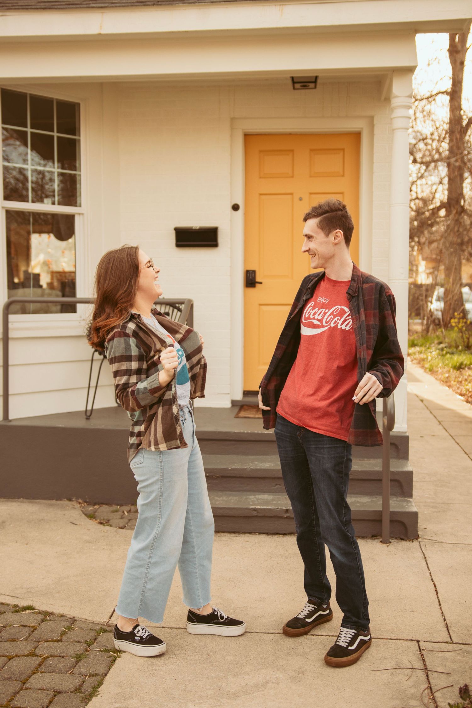 Two people in casual wear sharing a laugh on the front steps of a house.