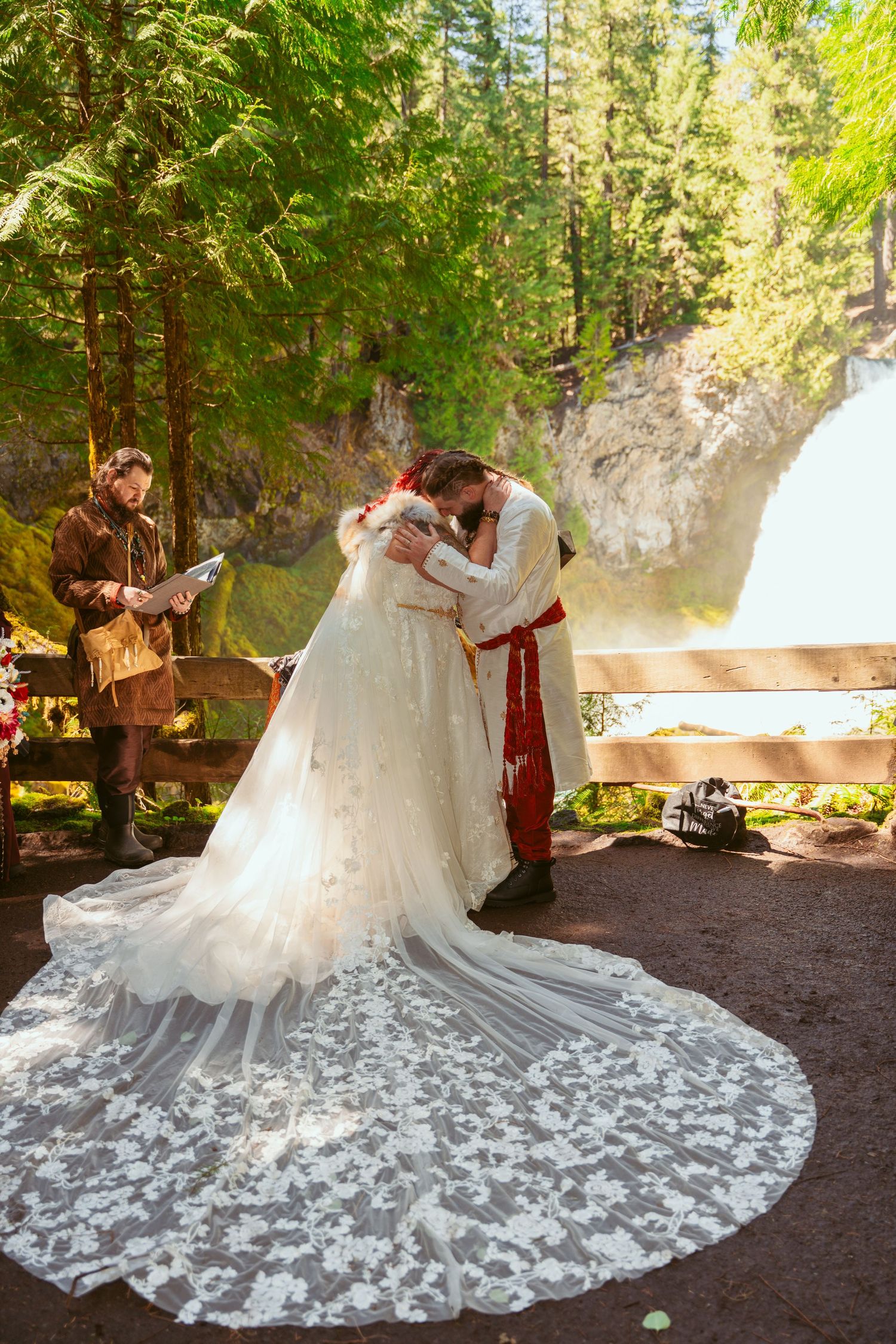 A stunning white wedding dress with an elaborate lace train spread out in a forest setting.