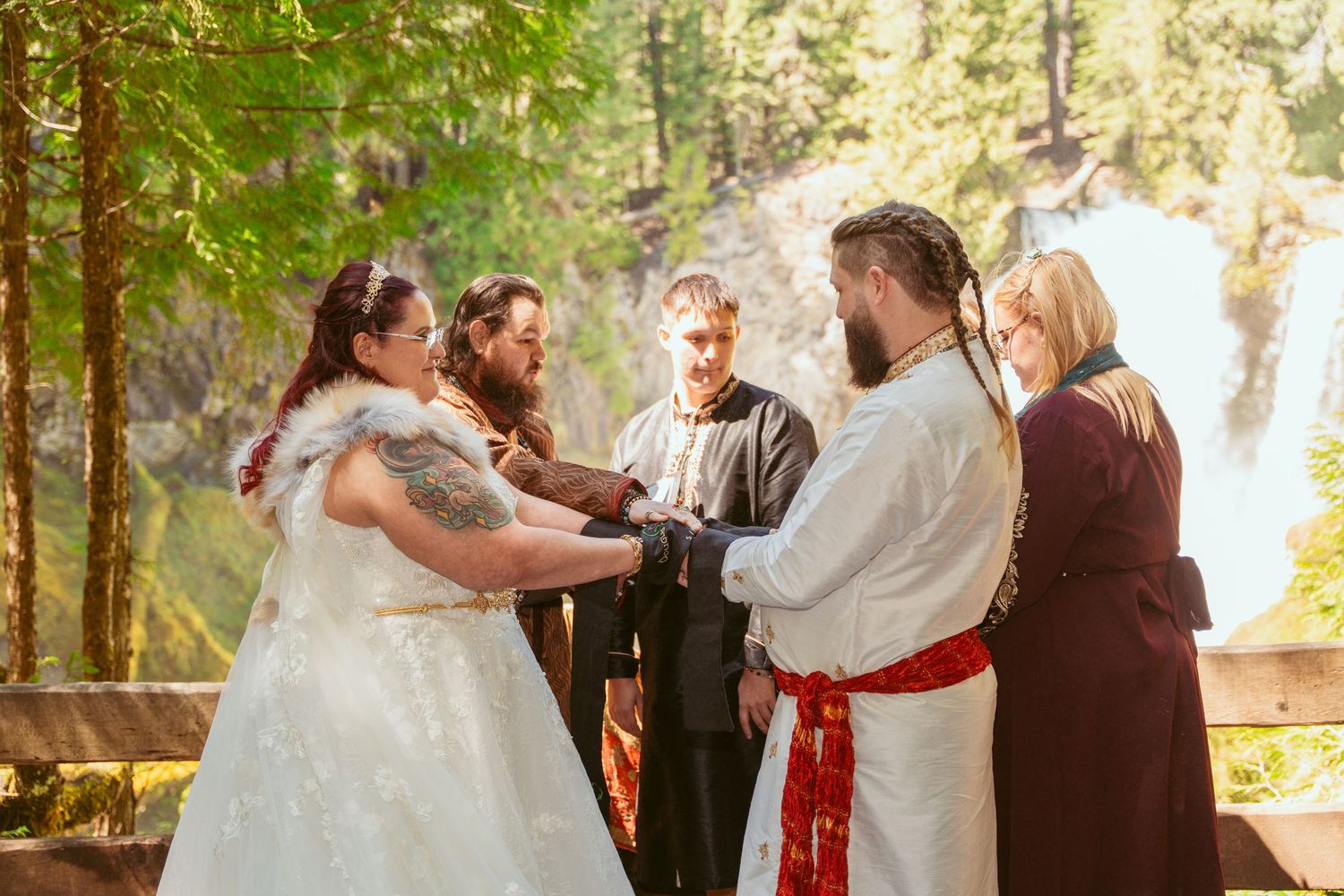 Wedding ceremony in a forest setting with white dress and red sash details.