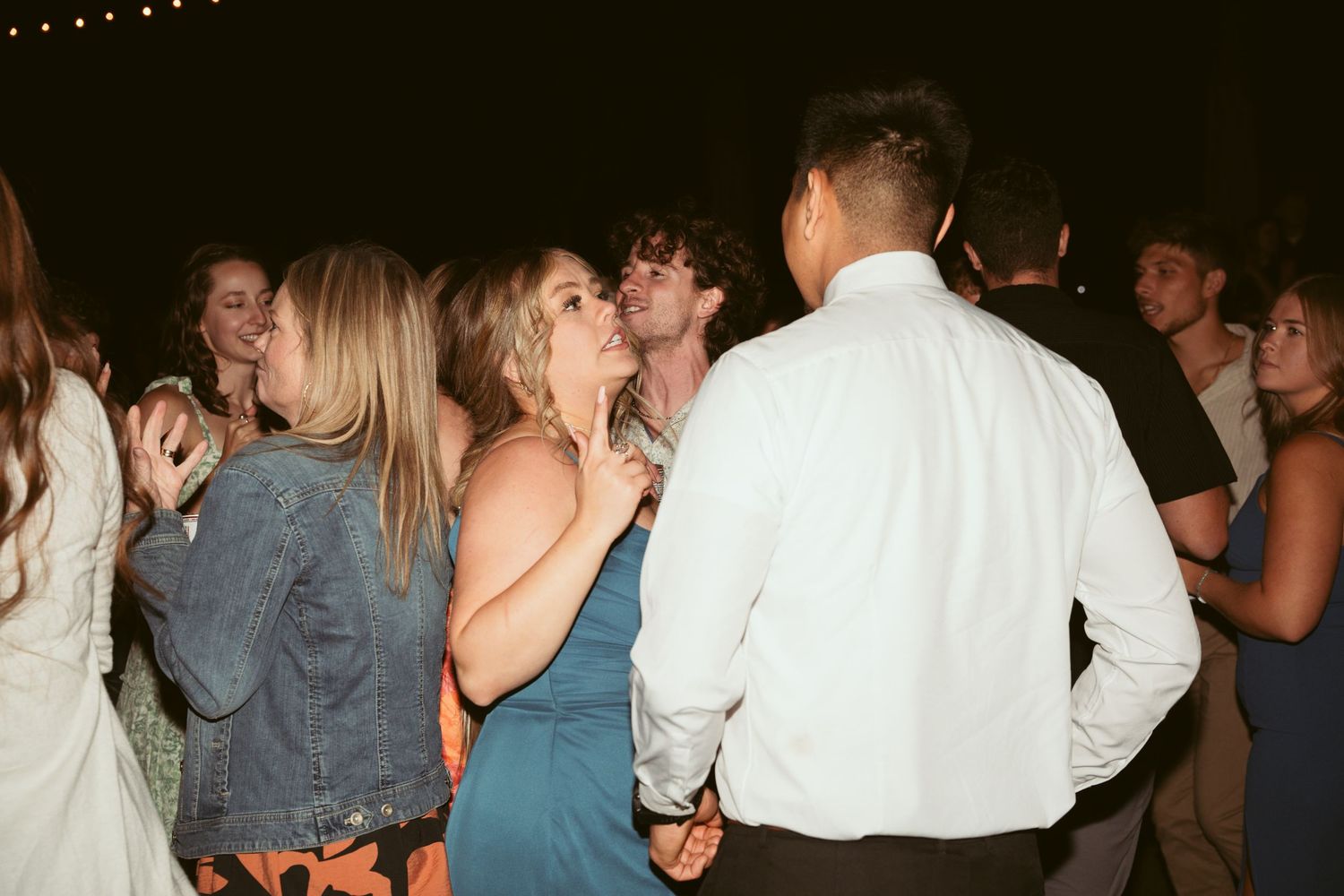 Party crowd dancing beneath strung lights at an outdoor evening event.