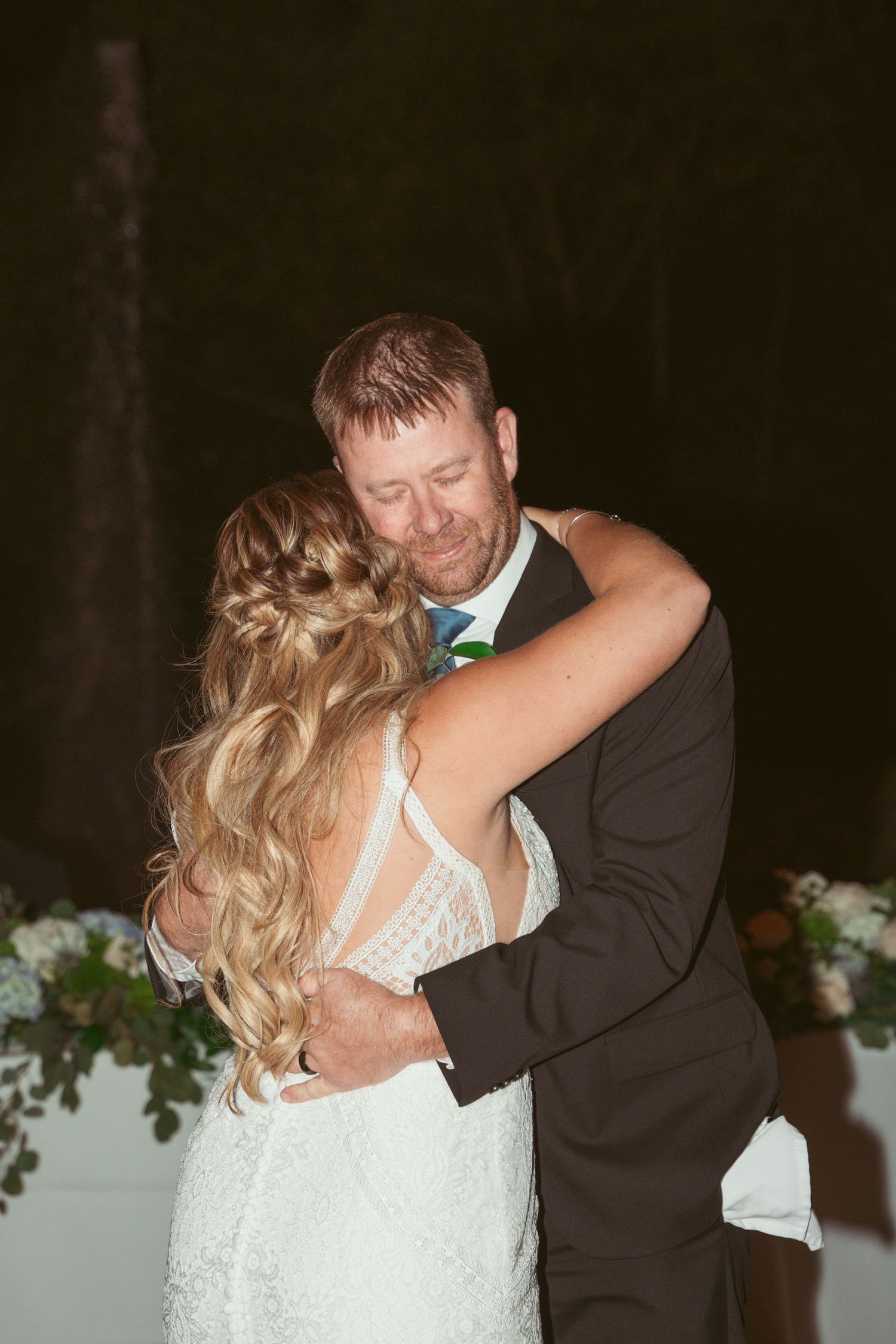 A romantic first dance between newlyweds at an evening wedding reception with floral decorations.