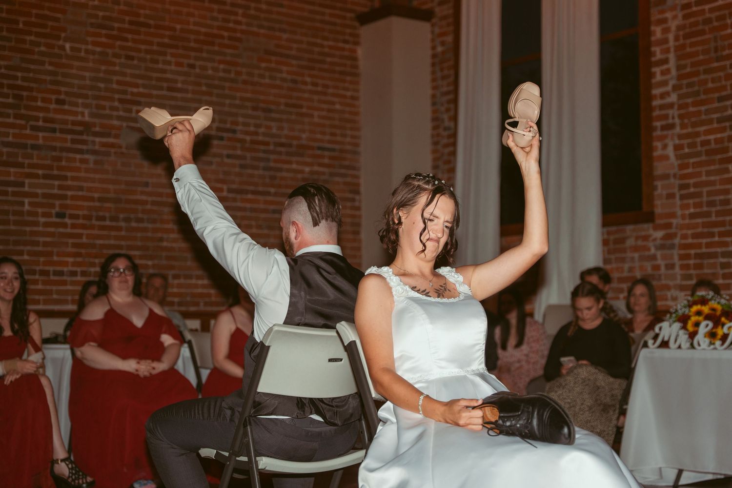 Wedding party members perform choreographed dance moves in a spacious brick-walled reception hall.
