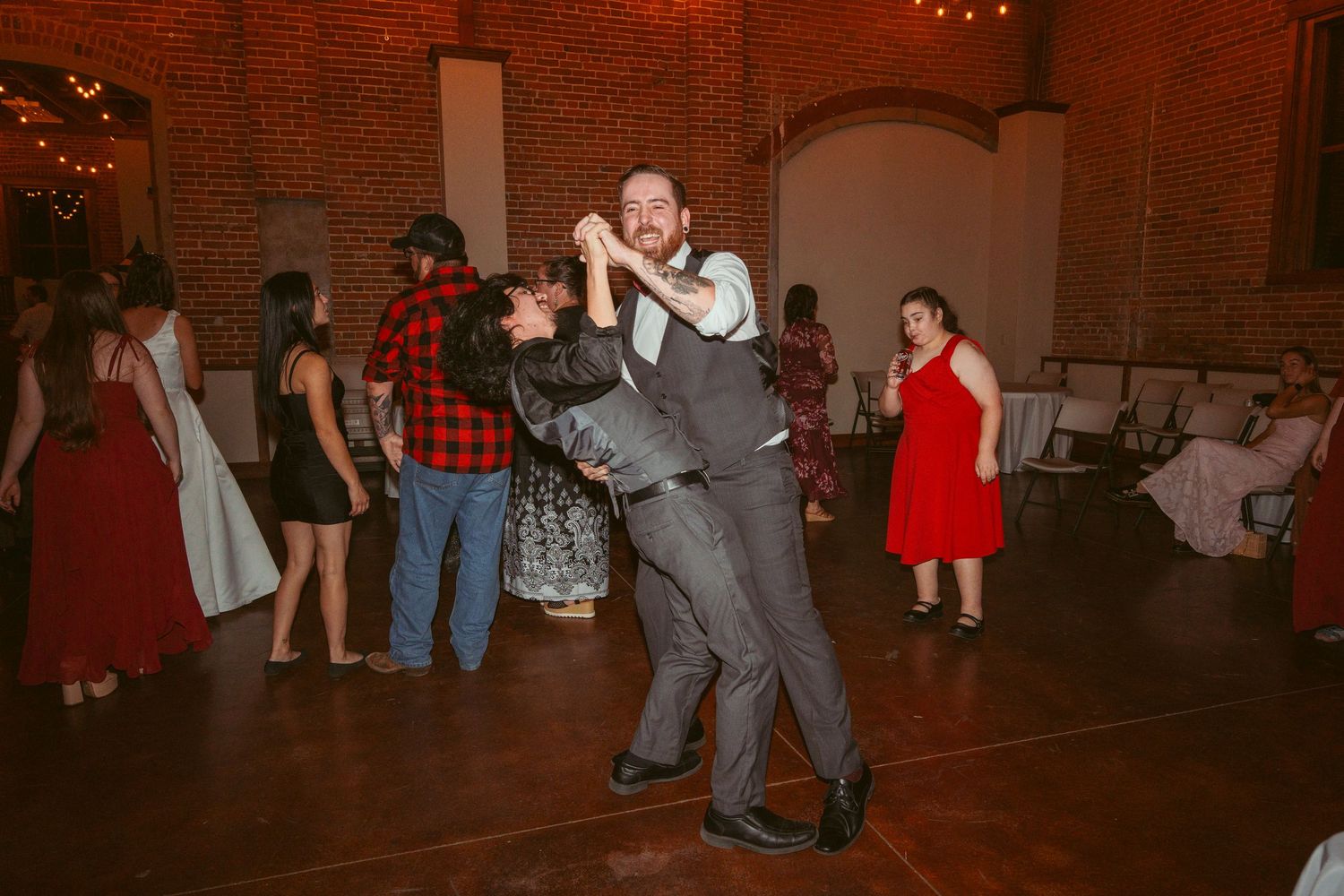 Dancers executing a dramatic dip move during a celebration in a brick-walled venue.
