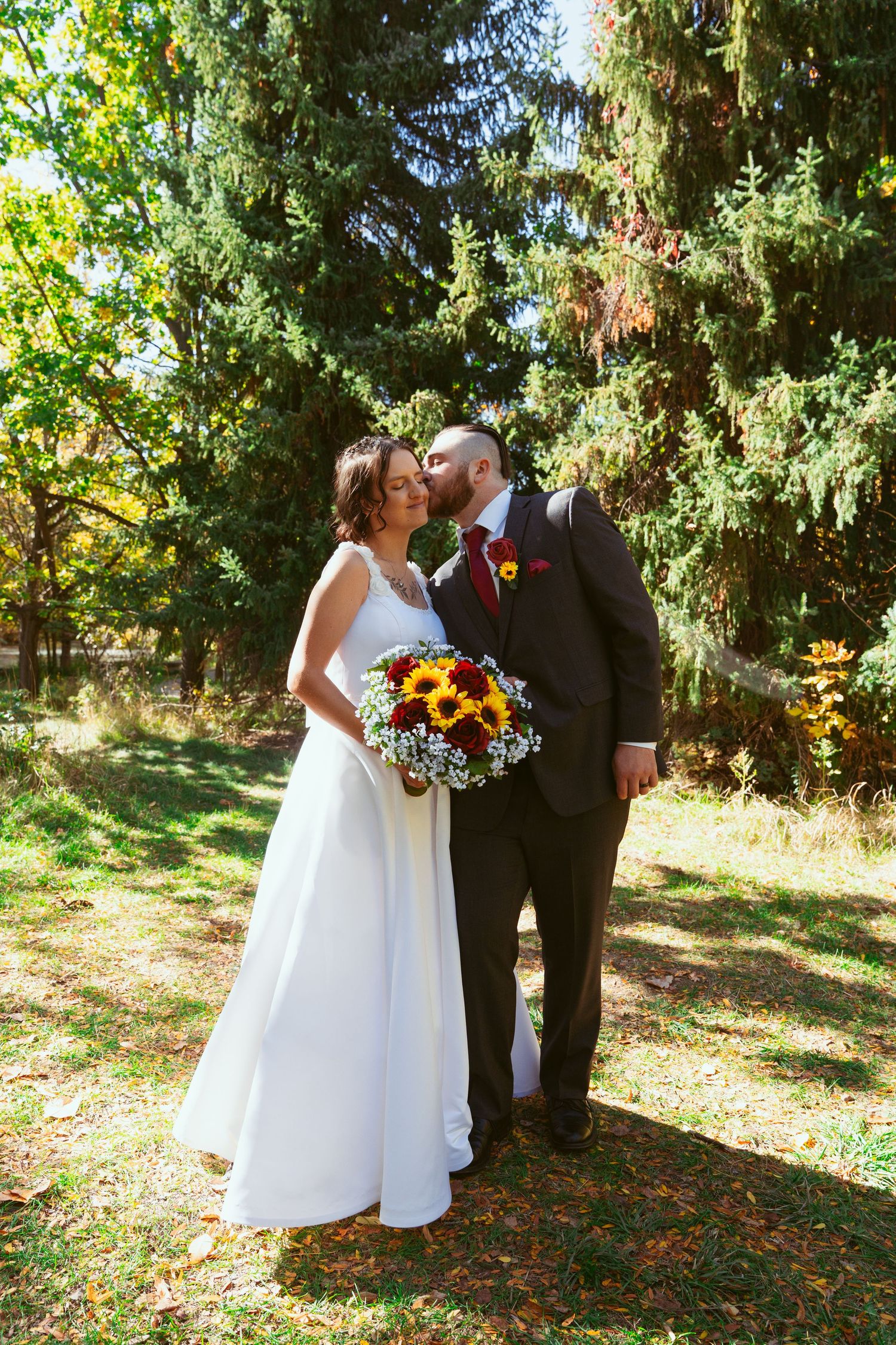 A wedding couple shares a tender moment in a forest setting with sunflowers in the bridal bouquet.