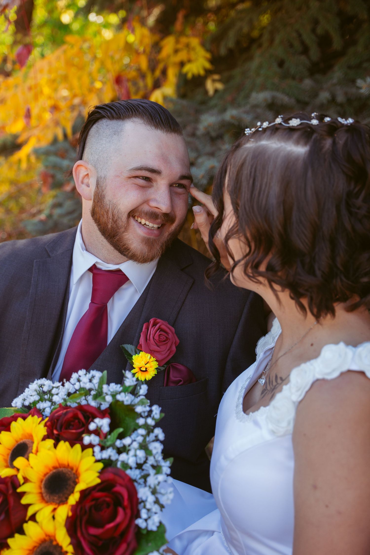 Autumn wedding portrait with sunflowers and burgundy accents against fall foliage.