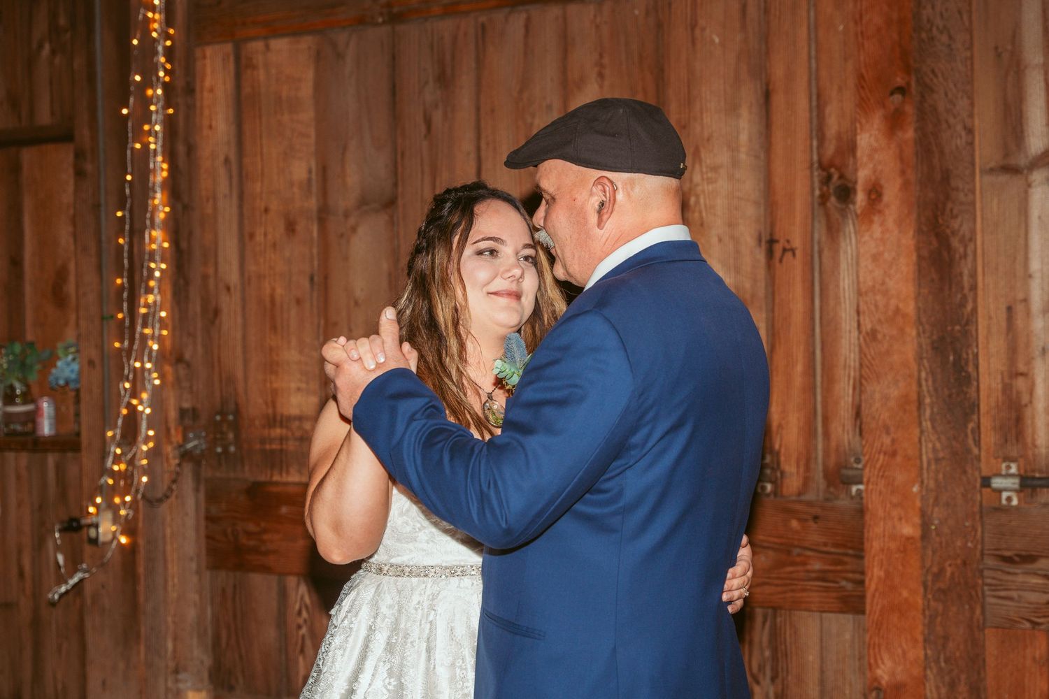 A couple dances closely in a rustic barn setting with warm lighting.