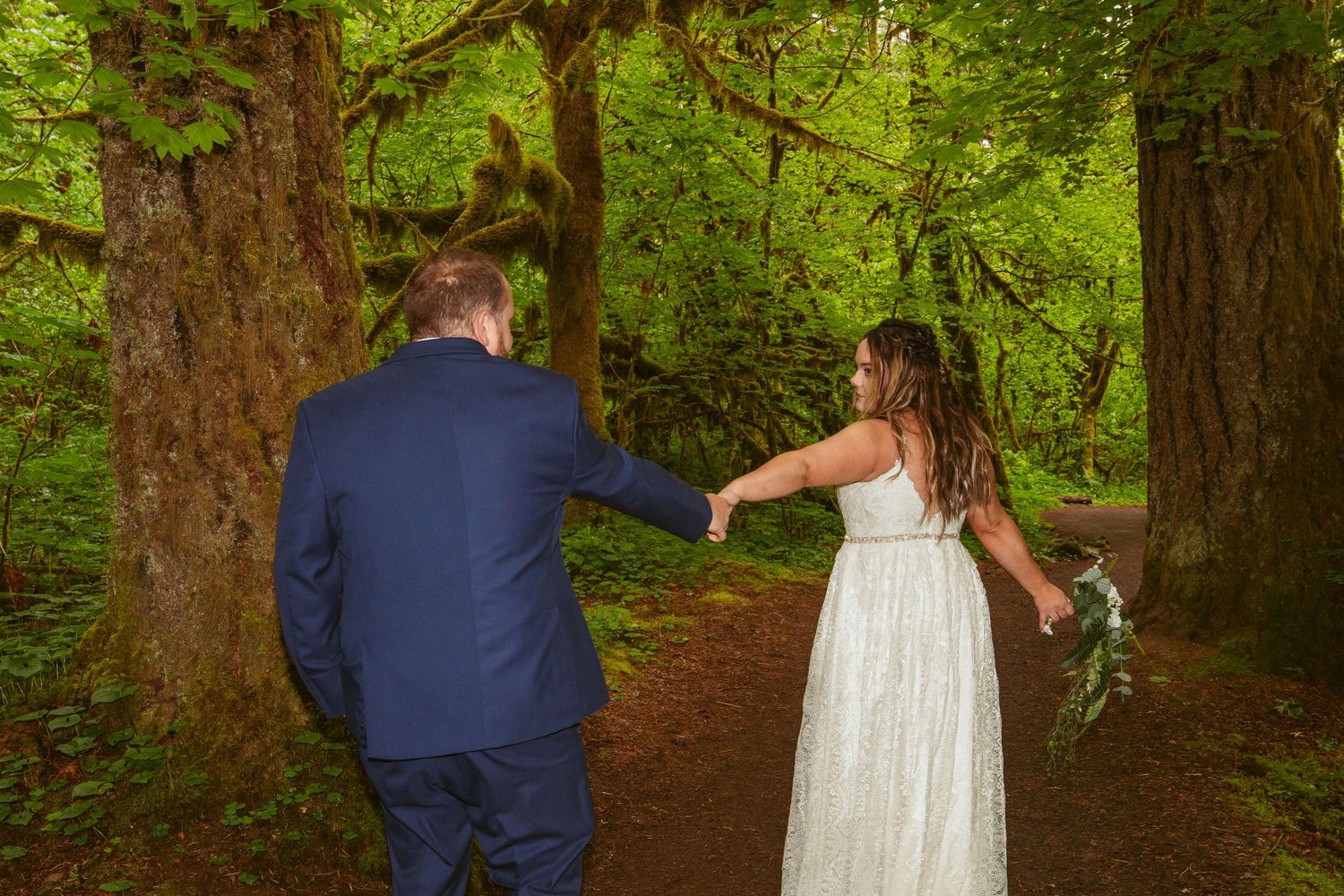 Bride and groom walk together through a peaceful forest setting.