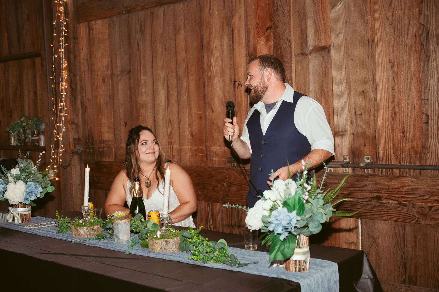 Wedding reception guests enjoying a casual moment in a rustic wooden barn setting with floral decorations.