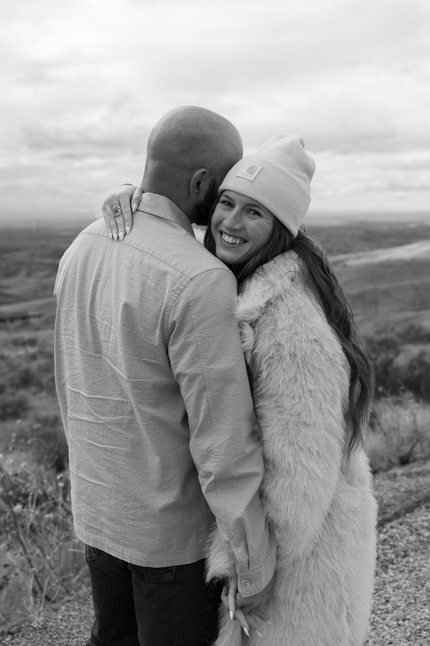 A couple embraces on a hilltop against a cloudy mountain landscape backdrop.