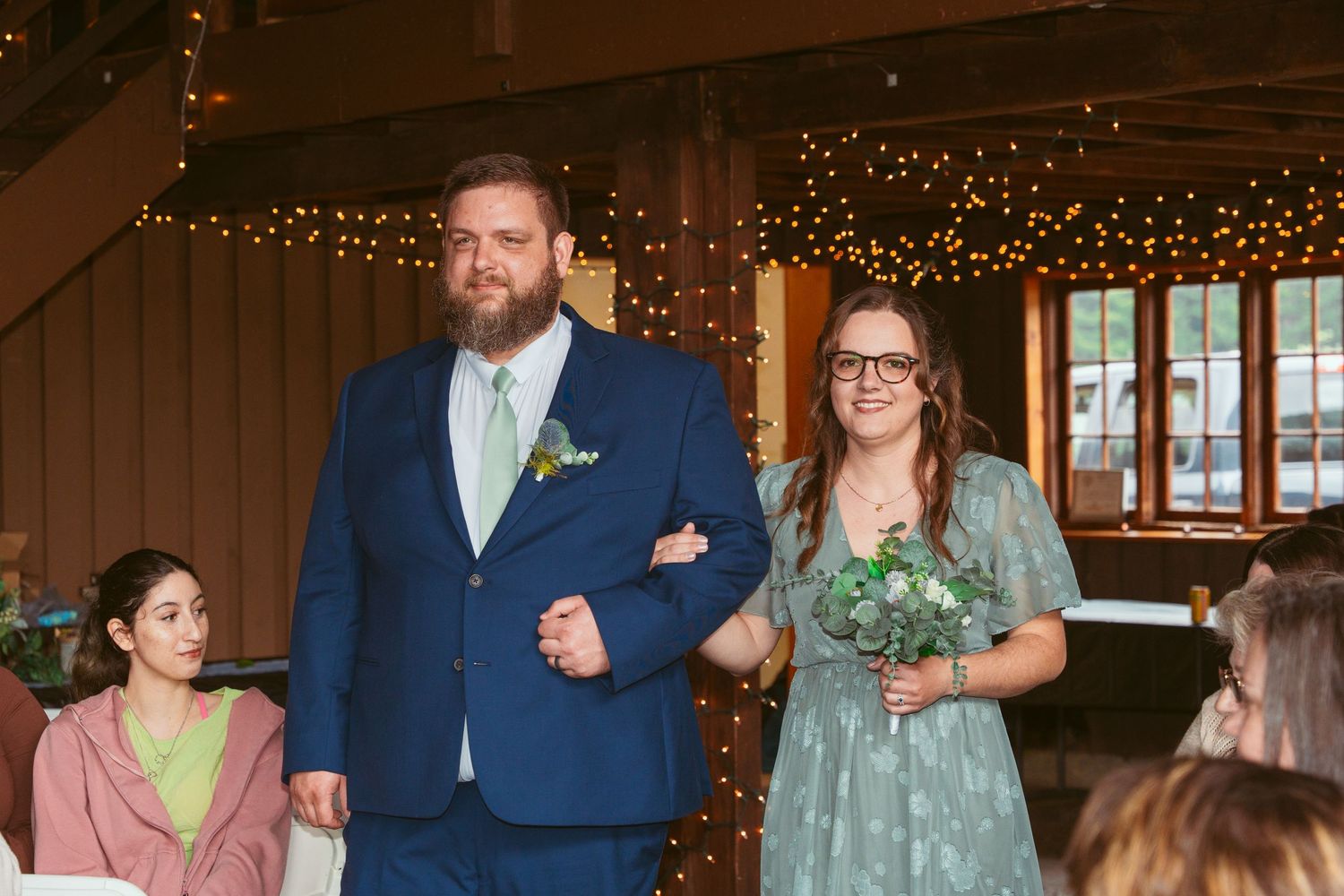 Wedding processional in rustic barn venue with wooden walls and fairy light decorations.